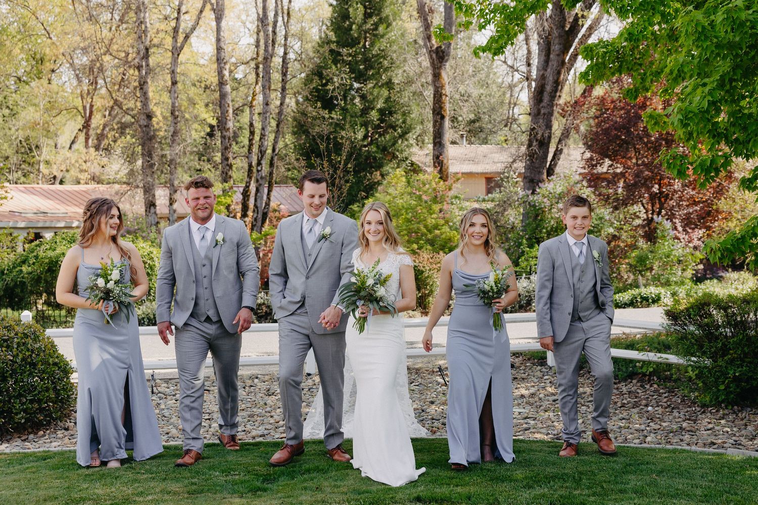 Wedding party poses outdoors wearing coordinated gray attire with bouquets.