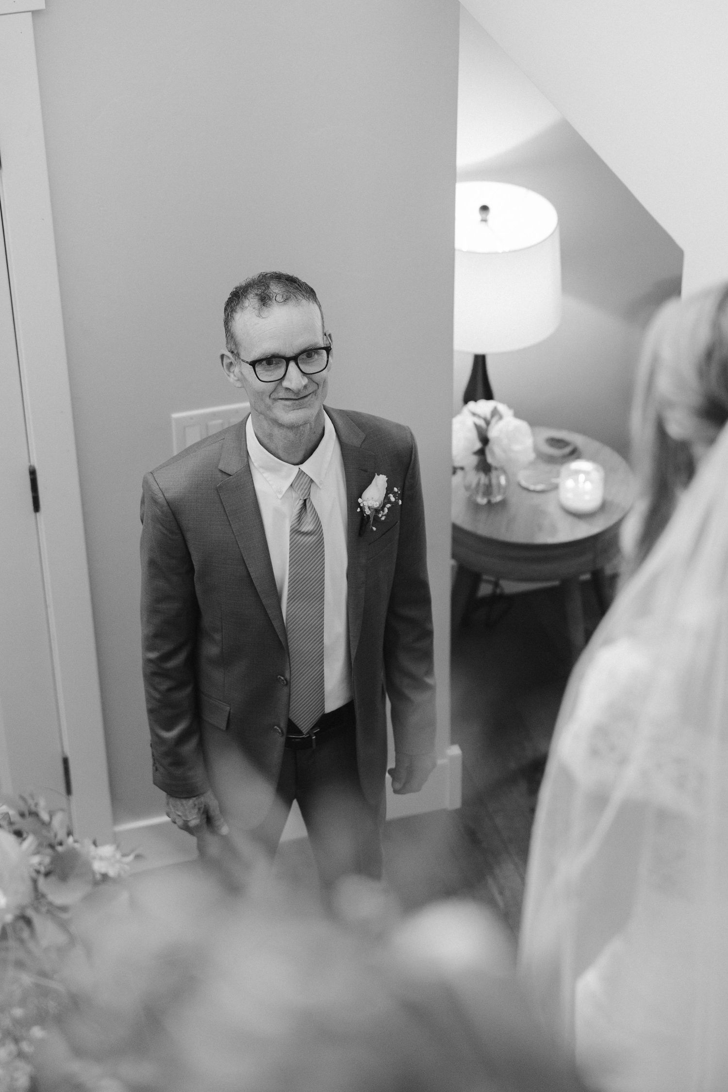 Groom in grey suit and glasses smiles during a pre-wedding first look moment.