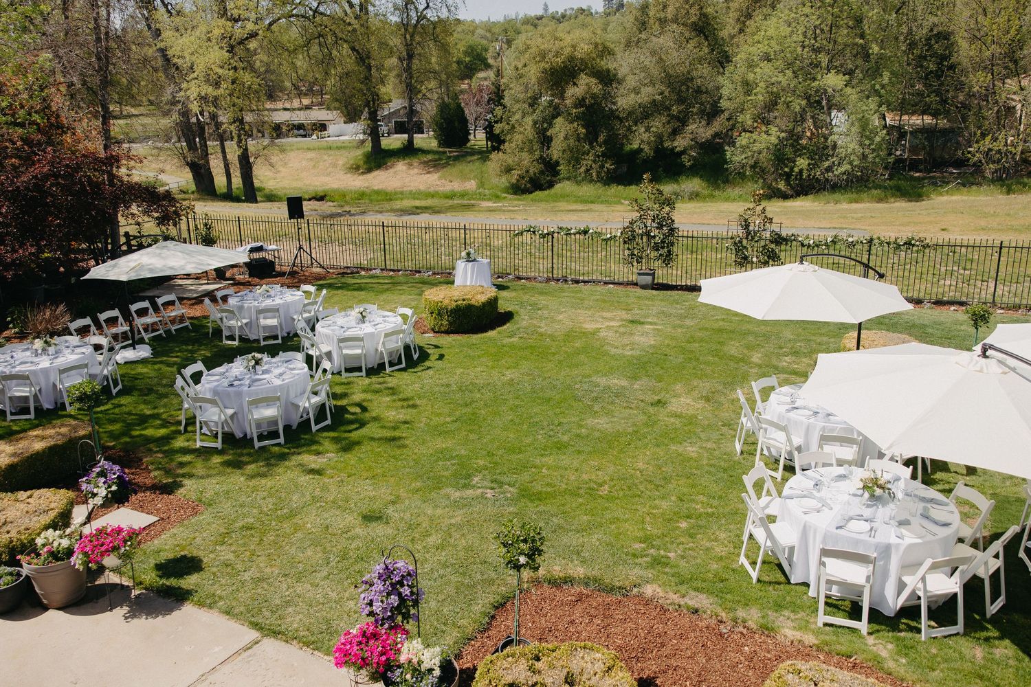 Outdoor wedding reception setup with white tents and round tables on a grassy lawn.