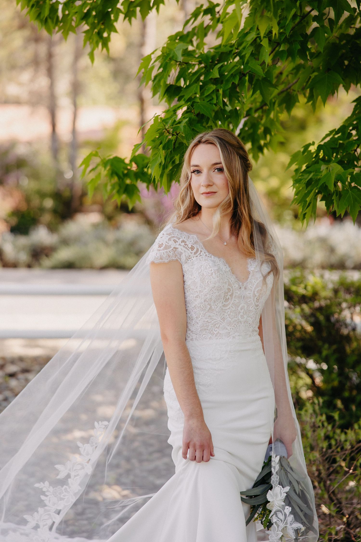 Elegant bridal portrait in garden setting with flowing veil and fitted lace gown.