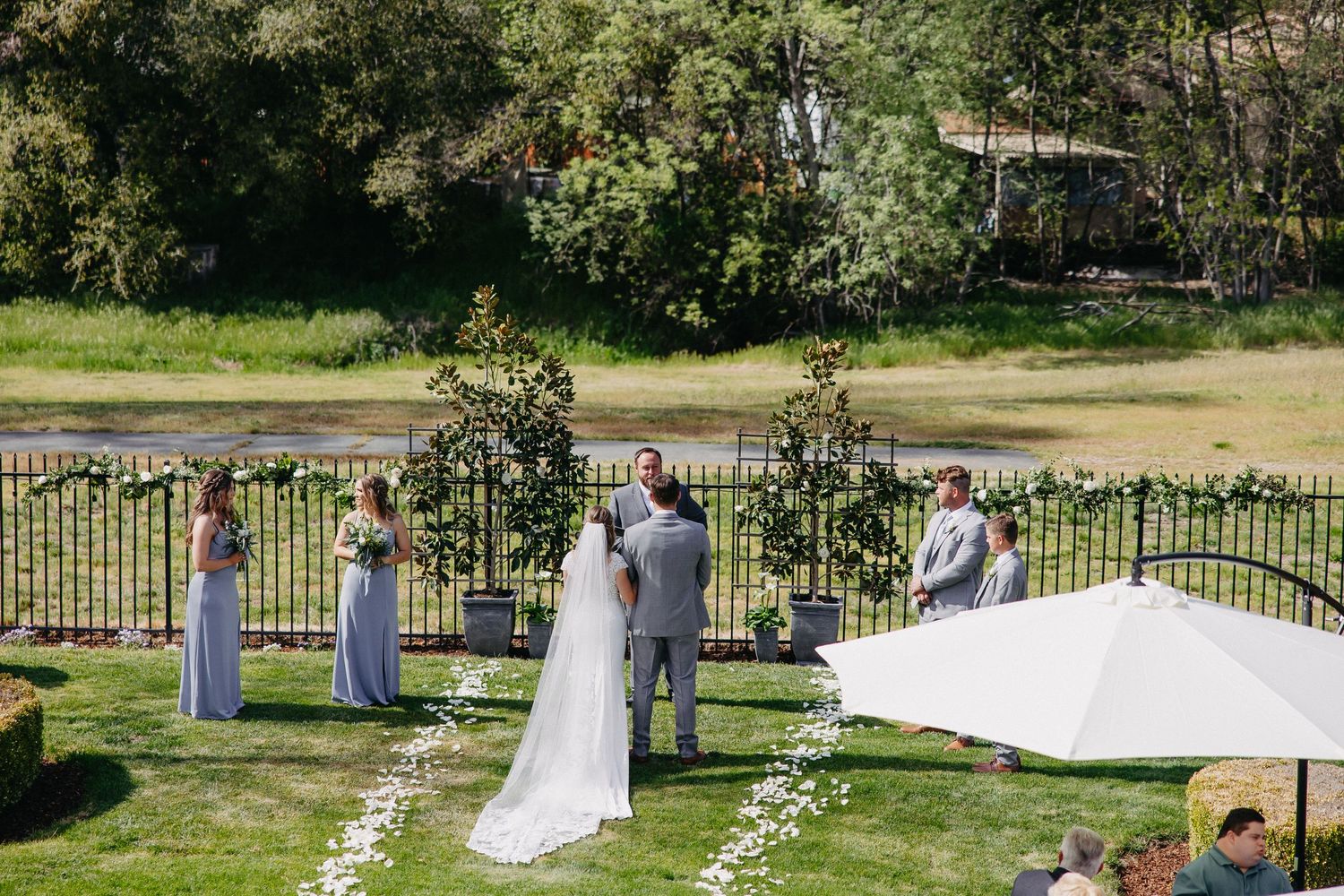 Garden wedding ceremony with flower-lined aisle and decorative iron fence backdrop.
