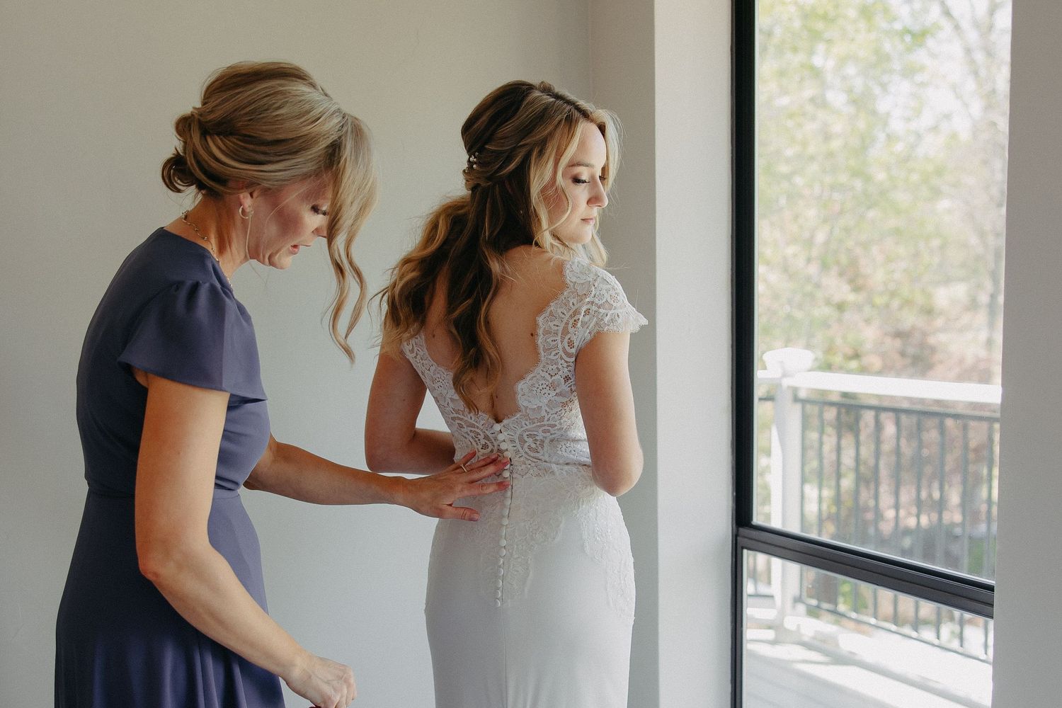 A tender moment of dress preparation by a window in natural light.