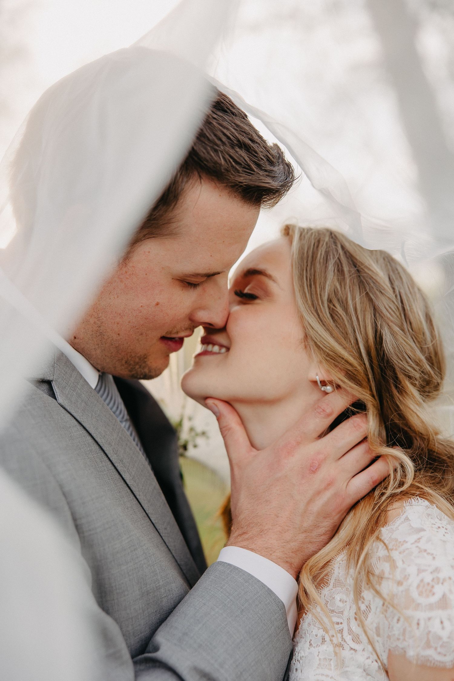 Romantic wedding photo of a couple sharing a tender moment under a flowing veil.