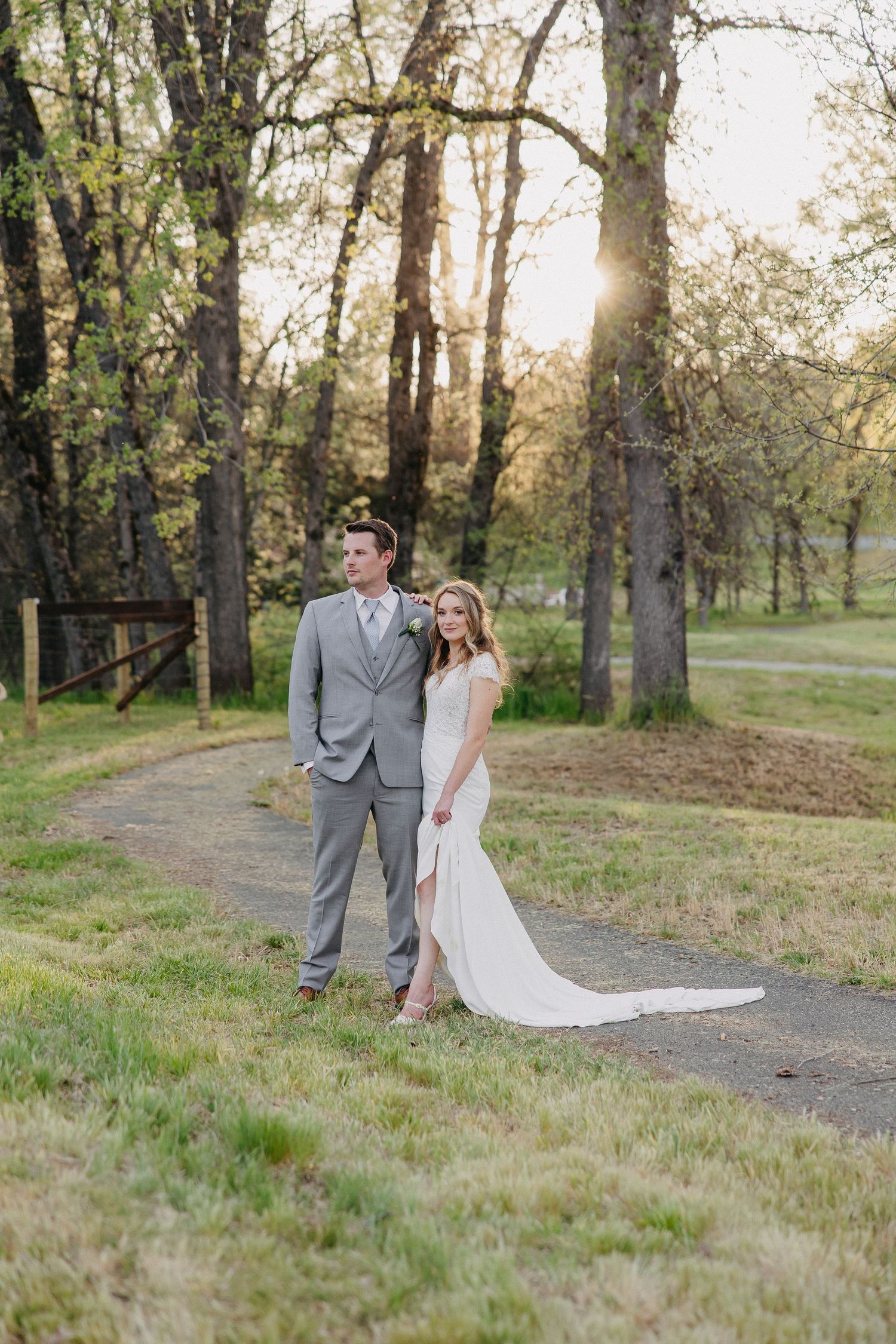 Newlyweds pose together on a nature trail surrounded by trees at sunset.