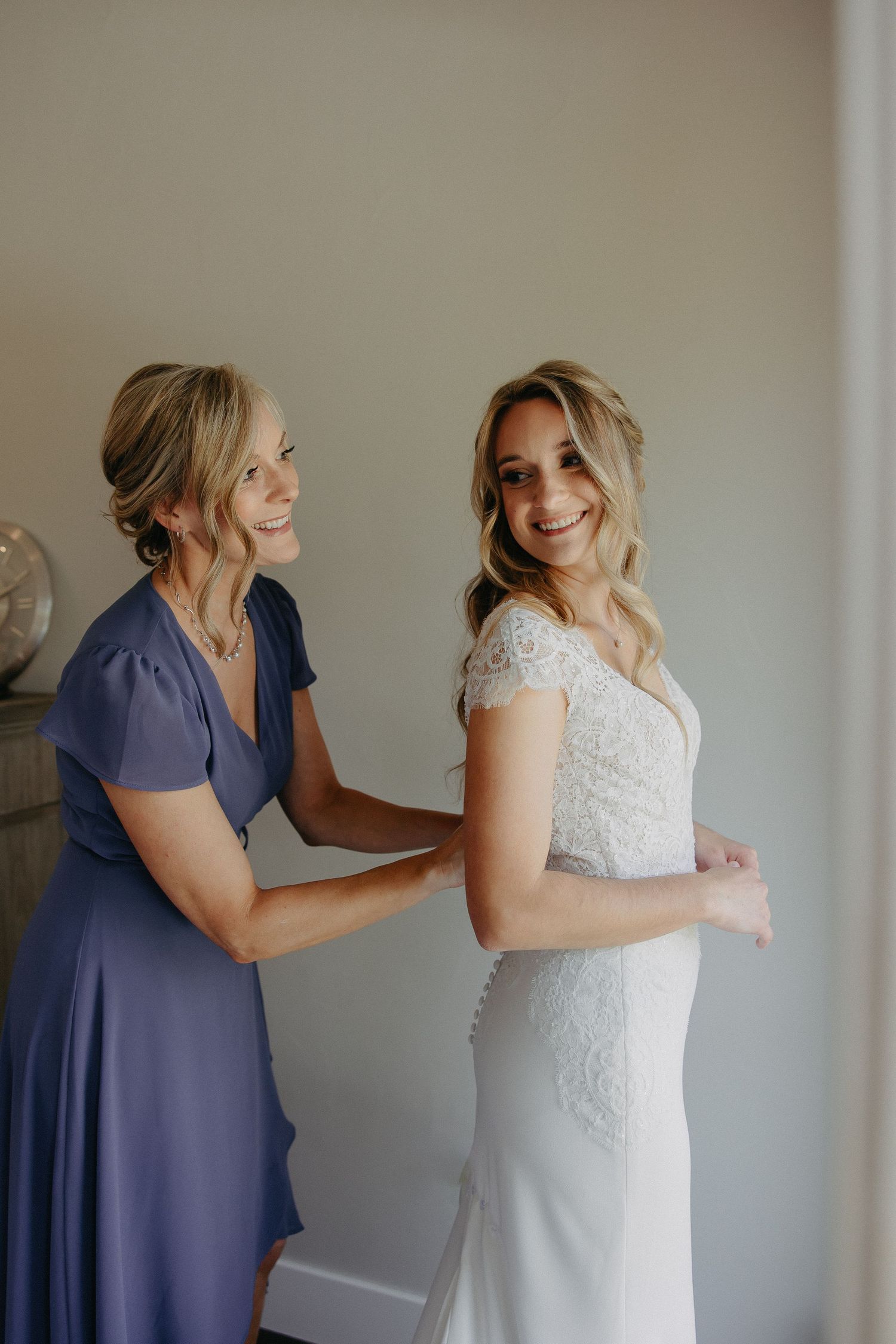 Joyful moment during wedding dress preparations with bridesmaid in navy helping with final touches.