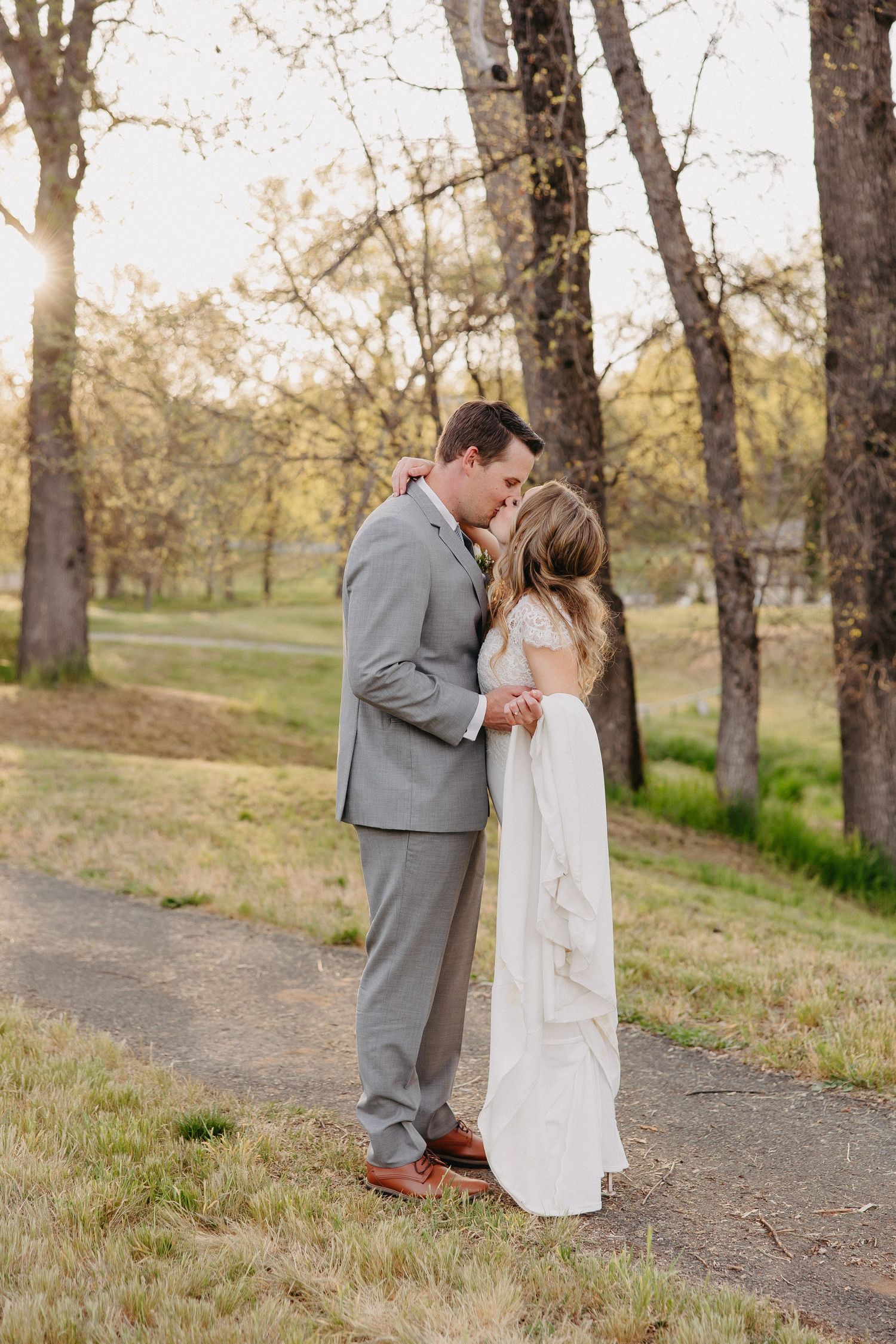 Romantic wedding photo of couple embracing on nature trail with soft lighting.
