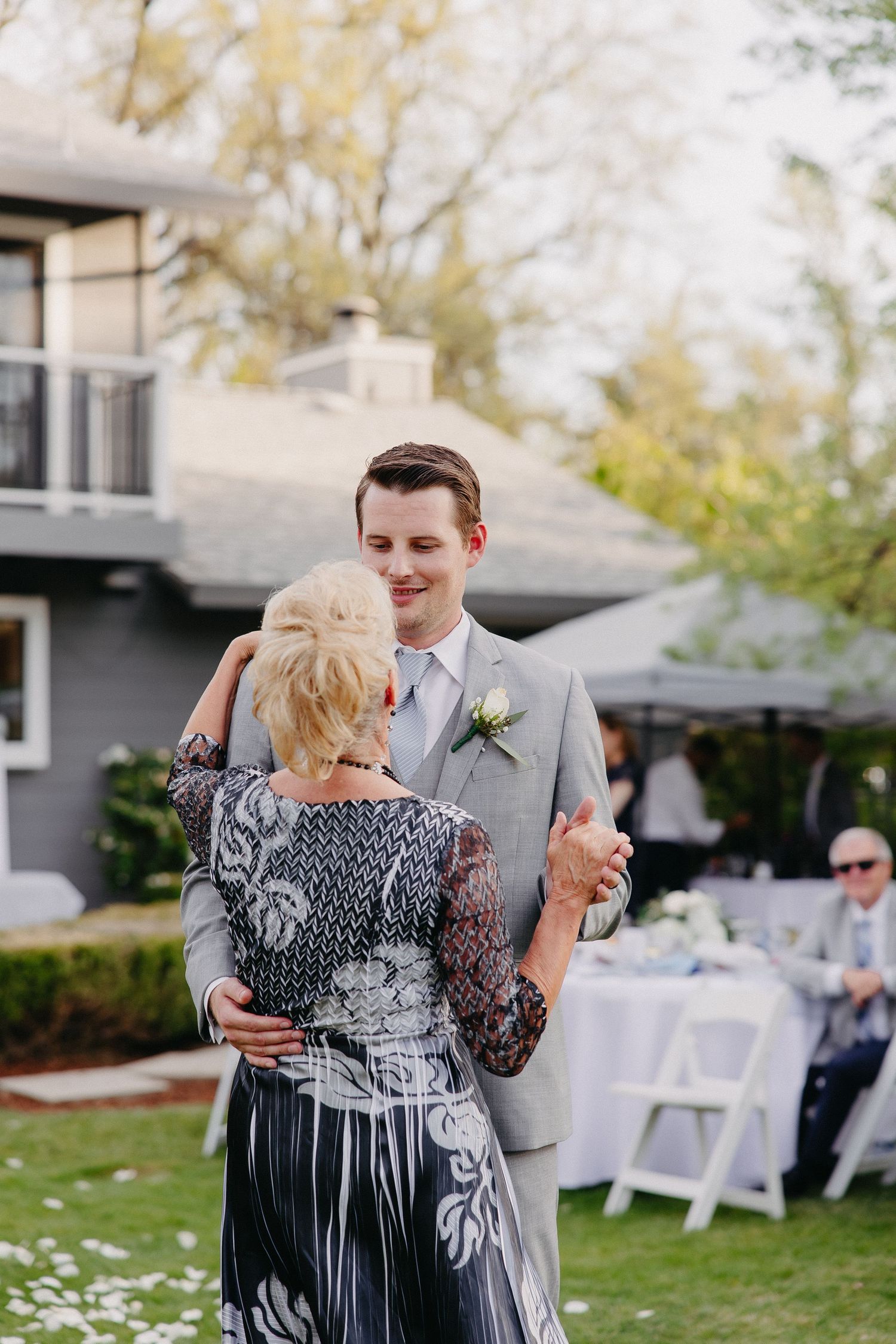 Wedding guests dancing at outdoor reception with grey suit and floral dress under garden umbrellas.