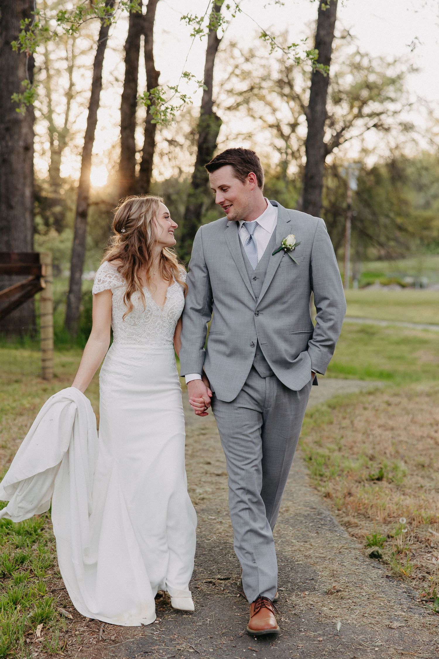 Couple walking hand in hand along woodland path during sunset wedding photoshoot.