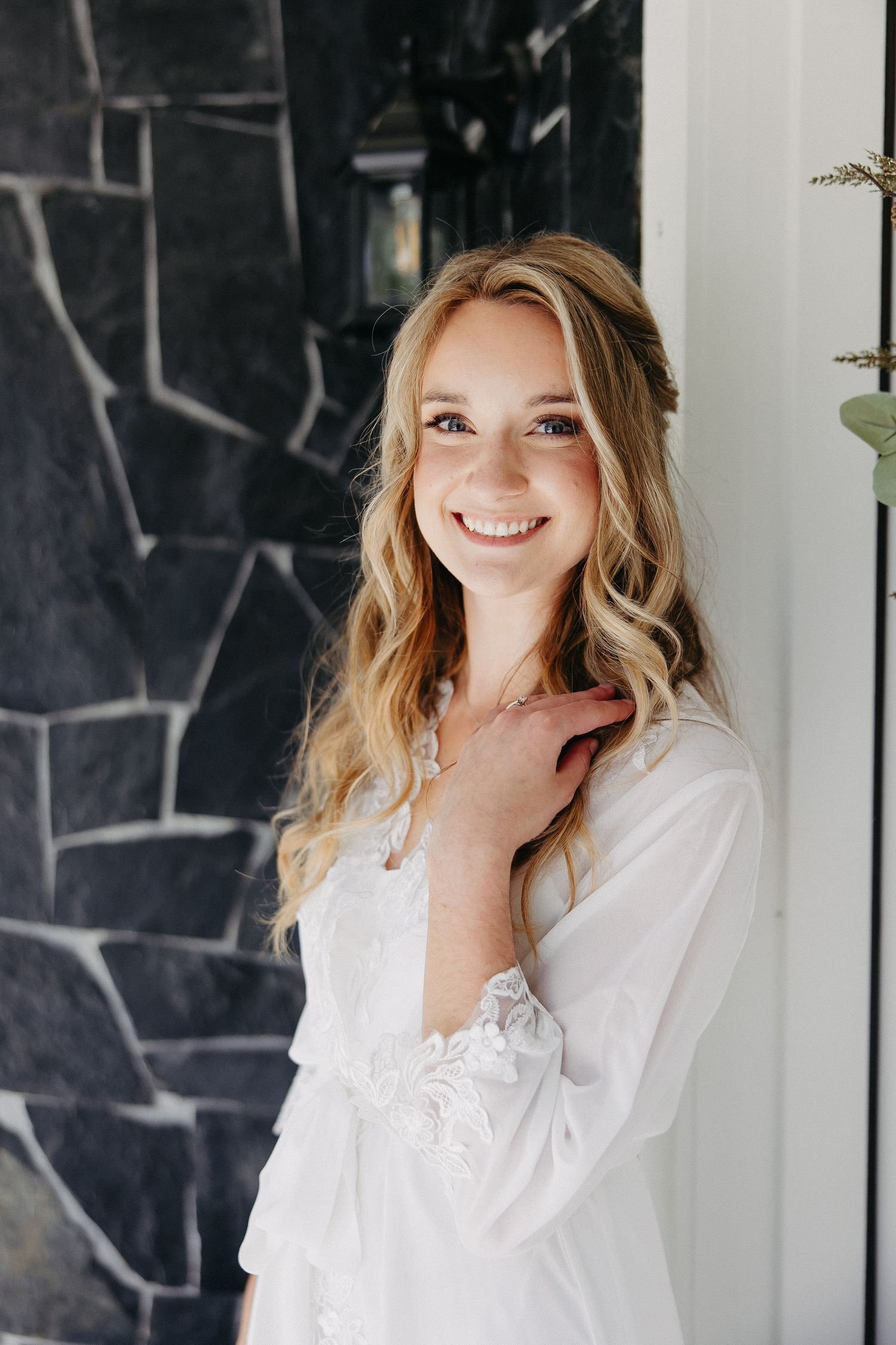 Ethereal bridal portrait against dark stone wall wearing white lace robe.