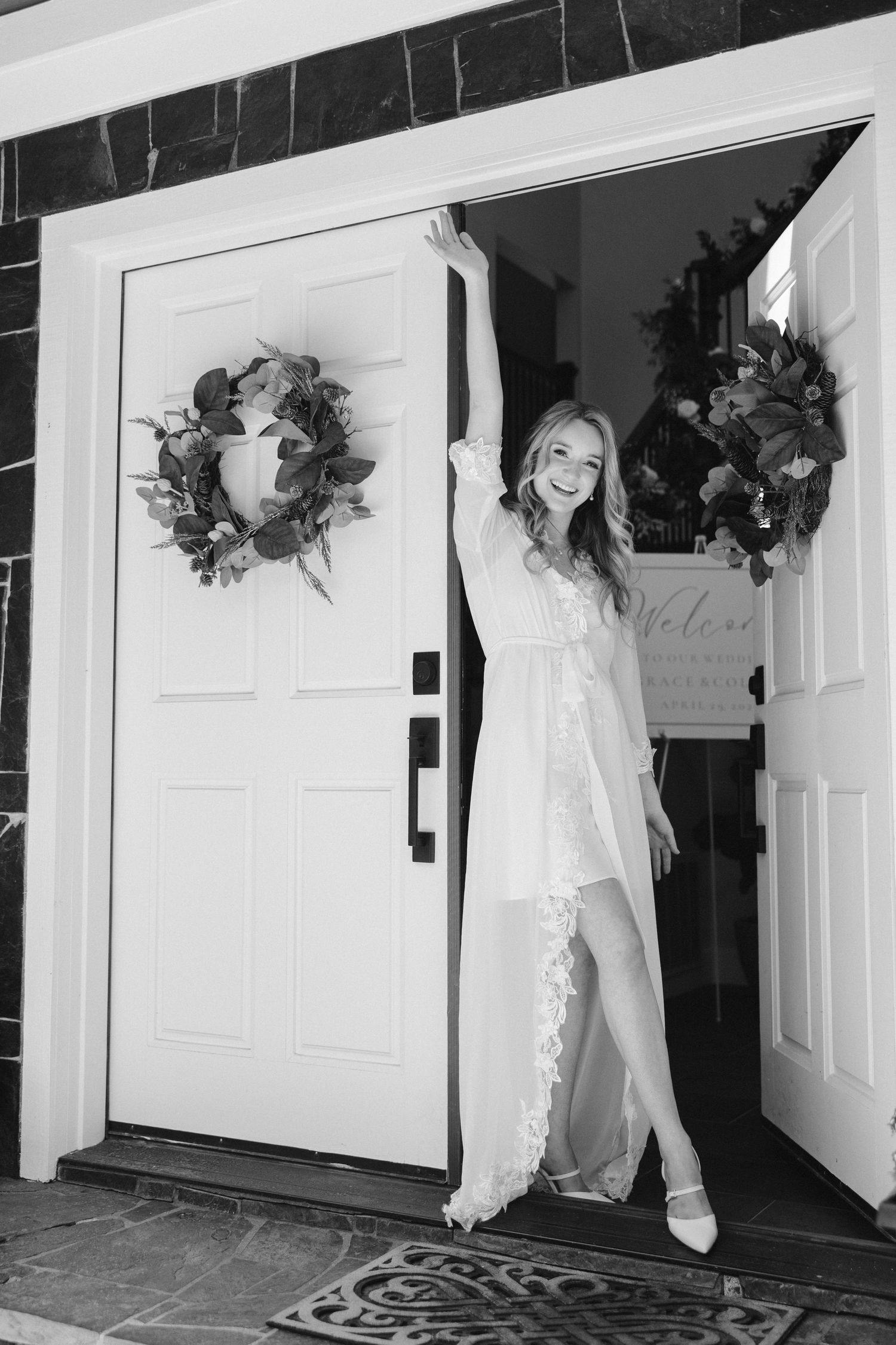 Black and white photo of bridal robe pose in doorway with decorative wreaths.