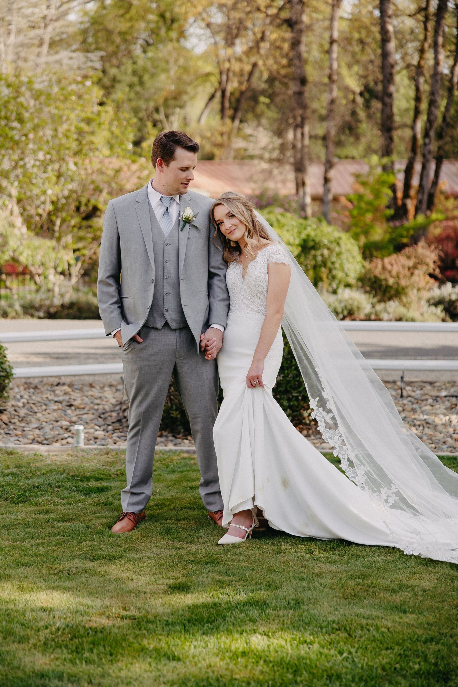 A playful wedding portrait of a couple standing together on landscaped grounds with autumn foliage.