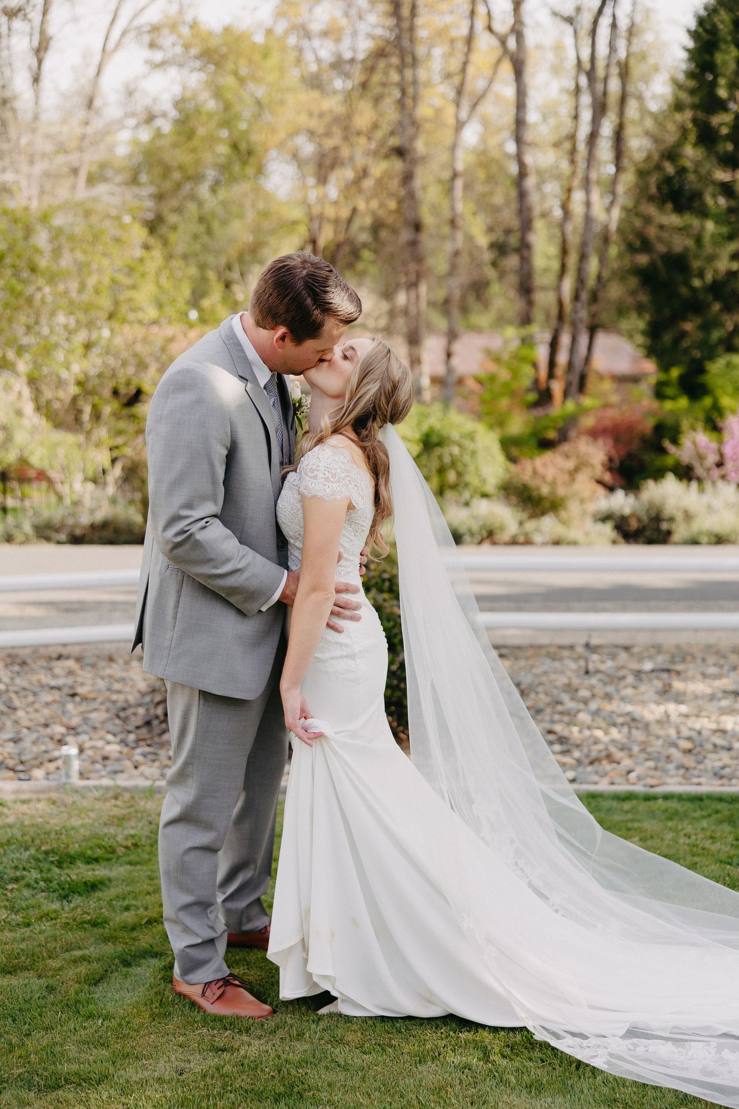 A romantic wedding couple sharing an intimate moment on manicured grounds with a long flowing veil.