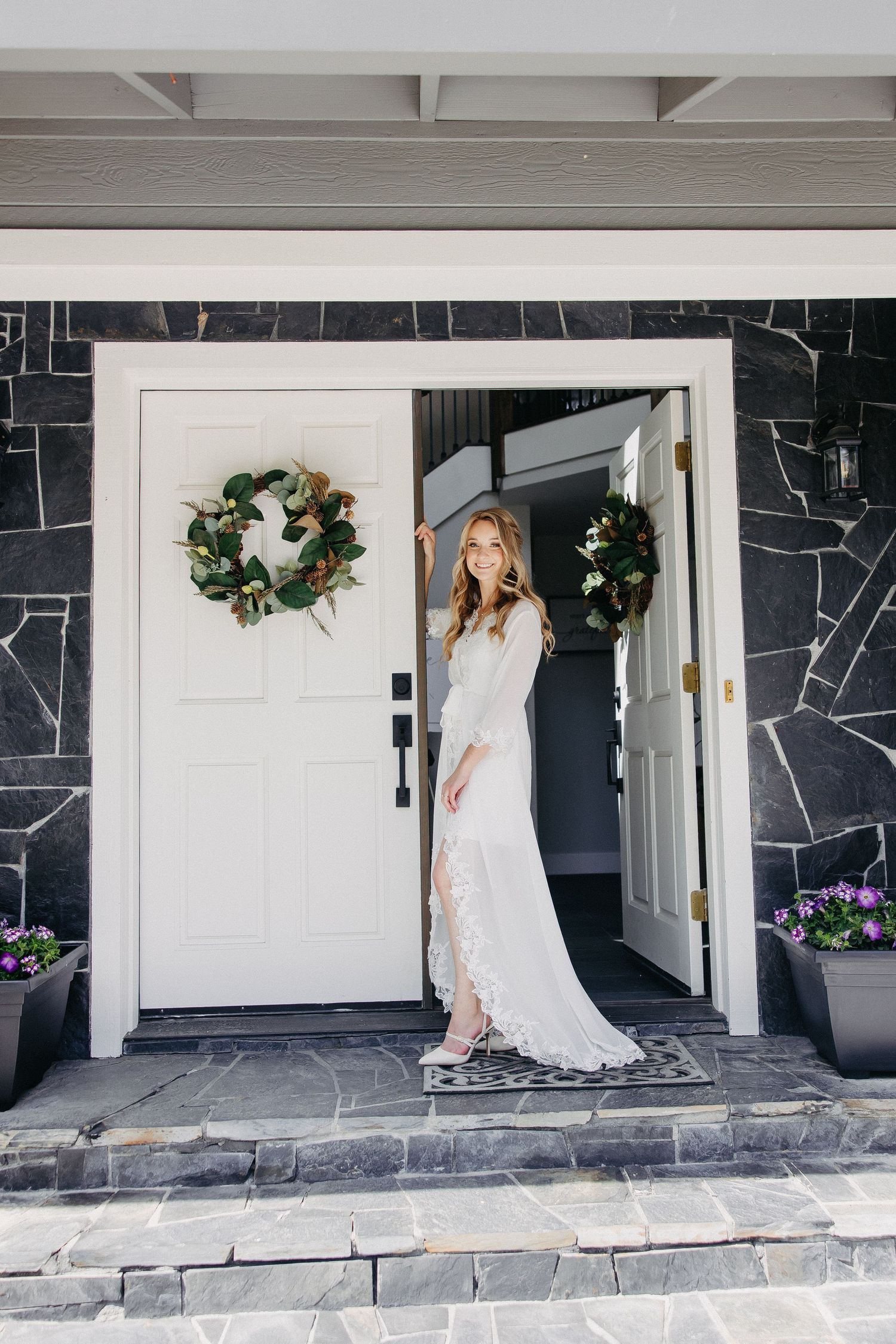 White wedding dress photographed in doorway with holiday wreaths and stone exterior.