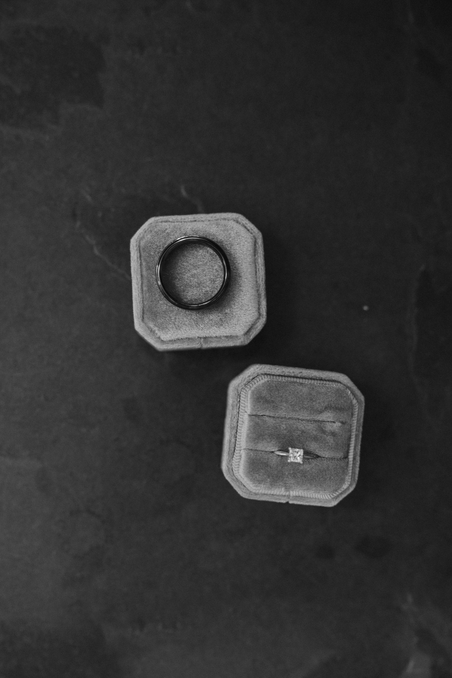 Two vintage gray velvet ring boxes on dark background in black and white.