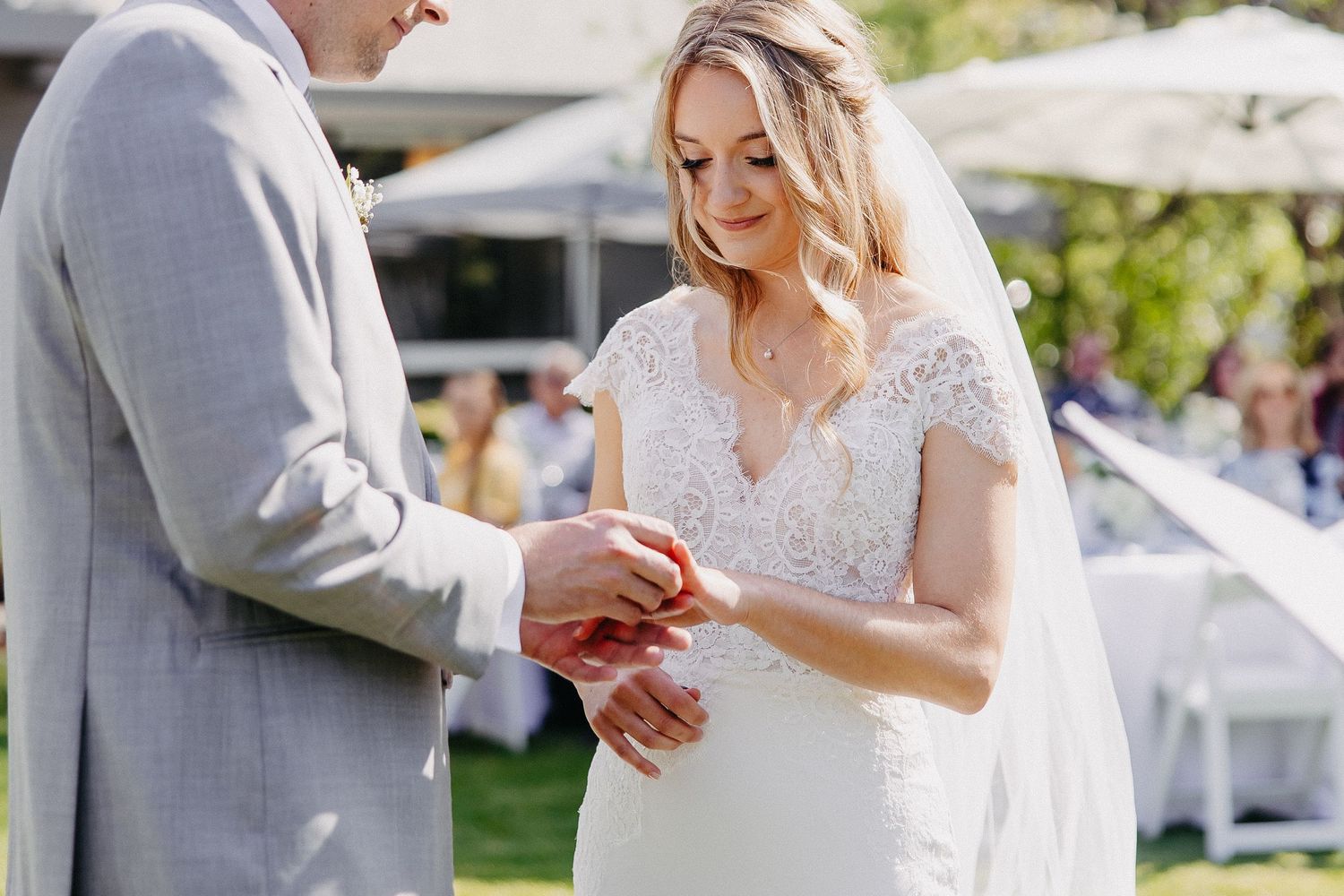 Close up of couple exchanging wedding rings during sunny outdoor ceremony.