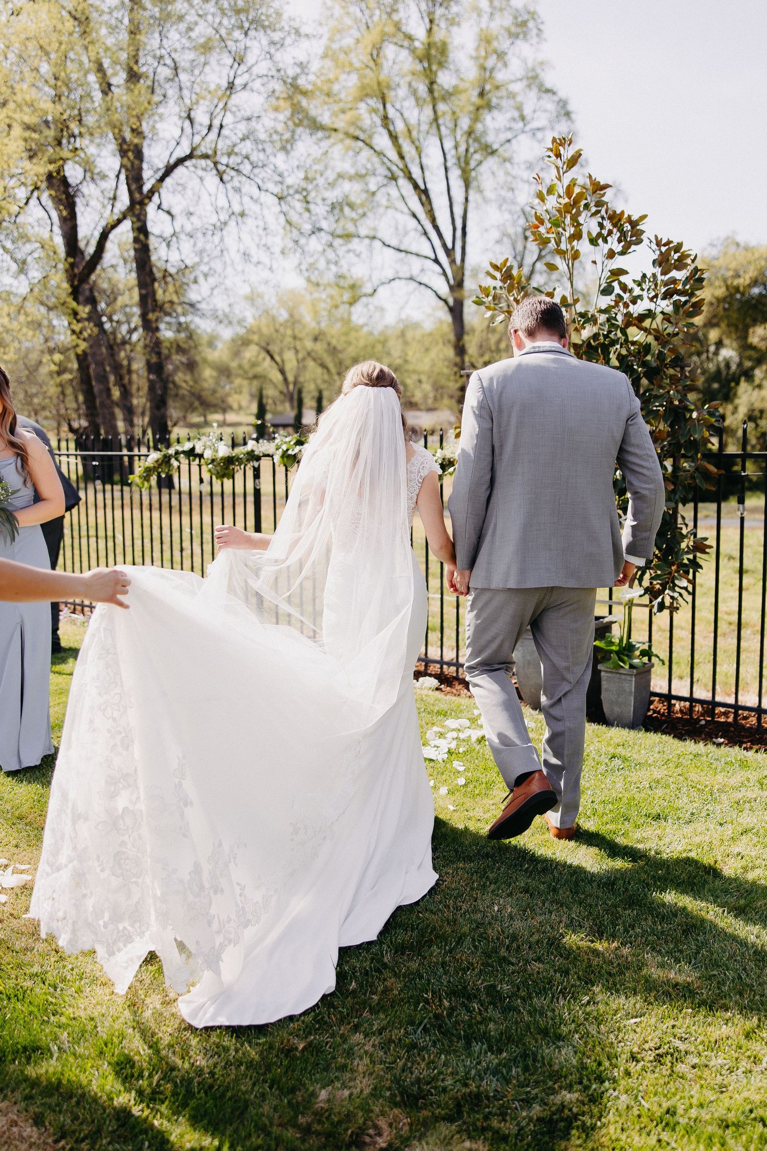 Wedding party walking across lawn with bride's flowing white dress train trailing behind.