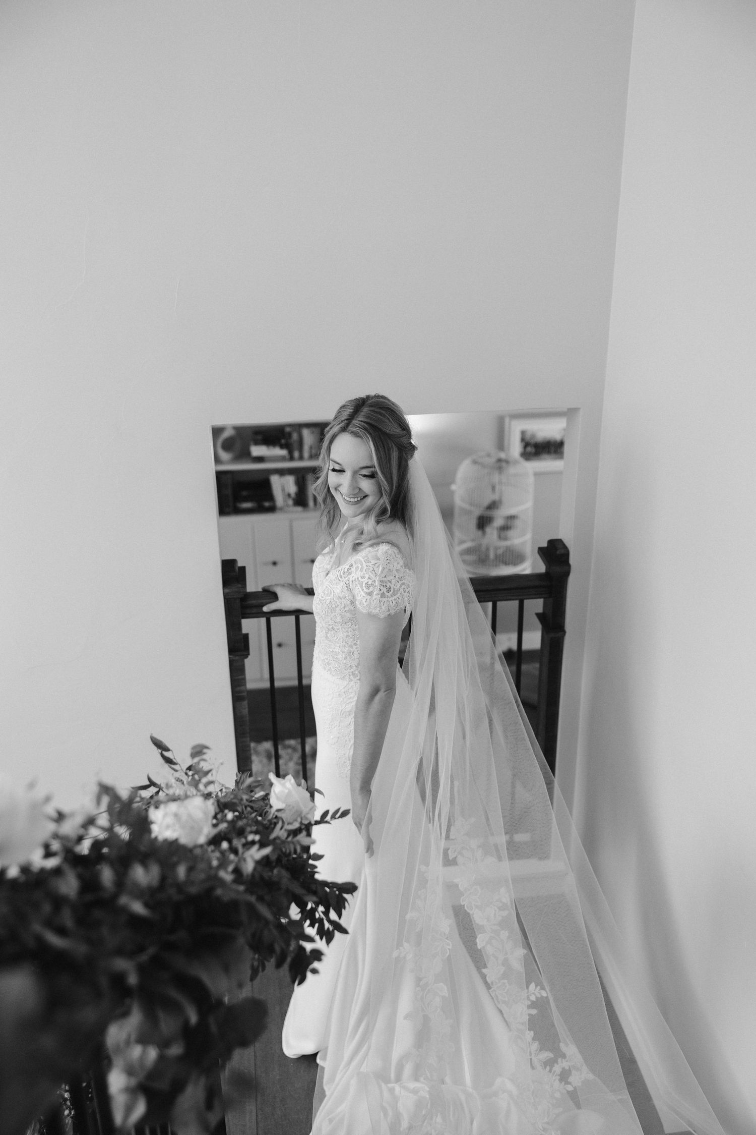 Bride in lace wedding dress and long veil poses elegantly in black and white photography.