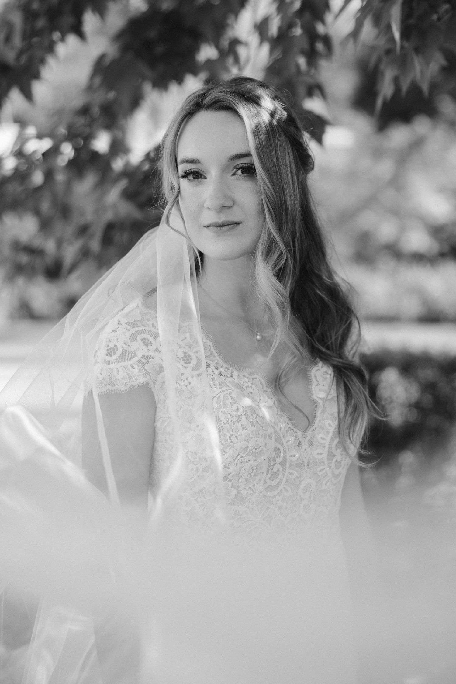 Black and white bridal portrait showcasing delicate lace details and soft lighting through leaves.