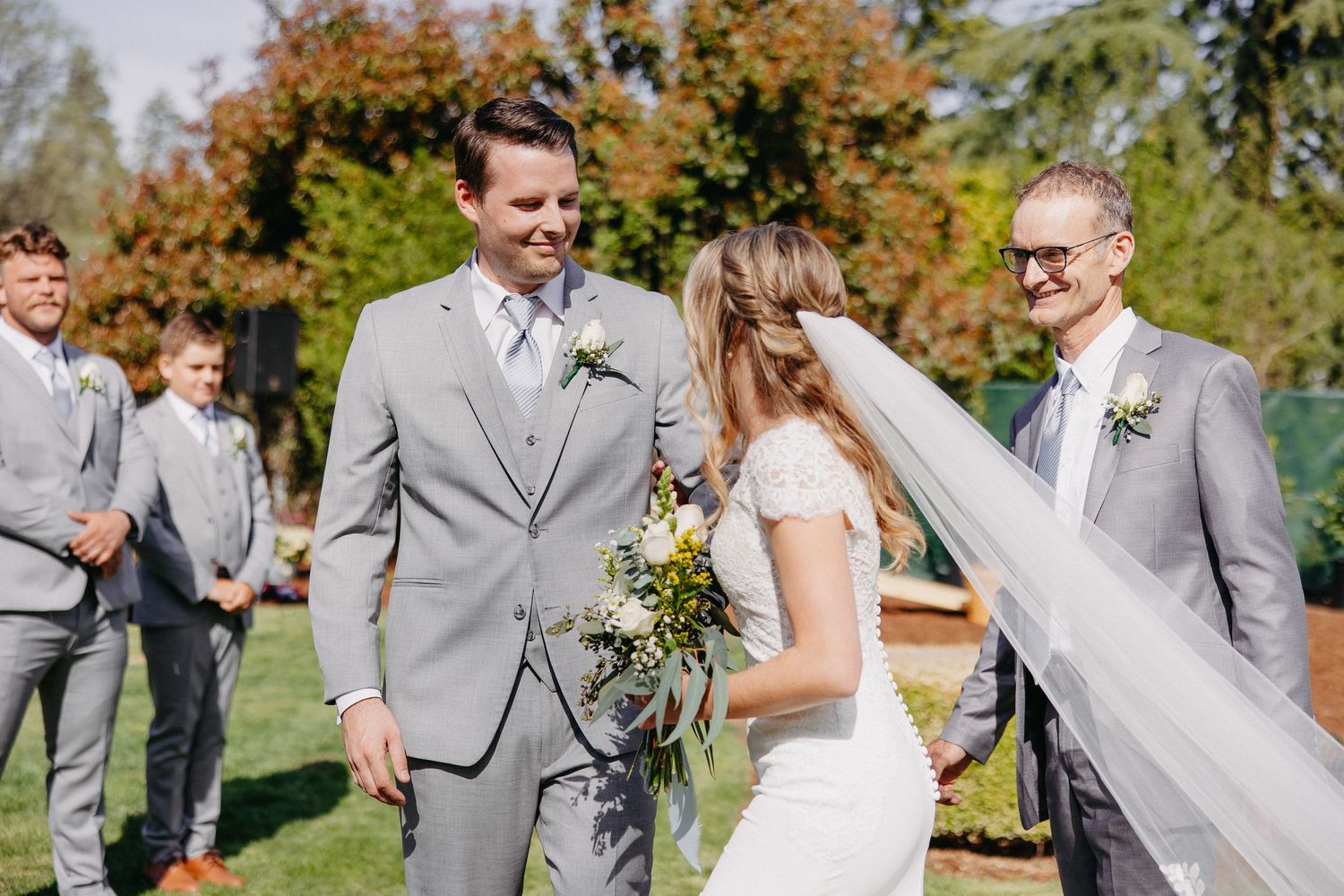 Sunny outdoor wedding ceremony in garden with autumn foliage in background.