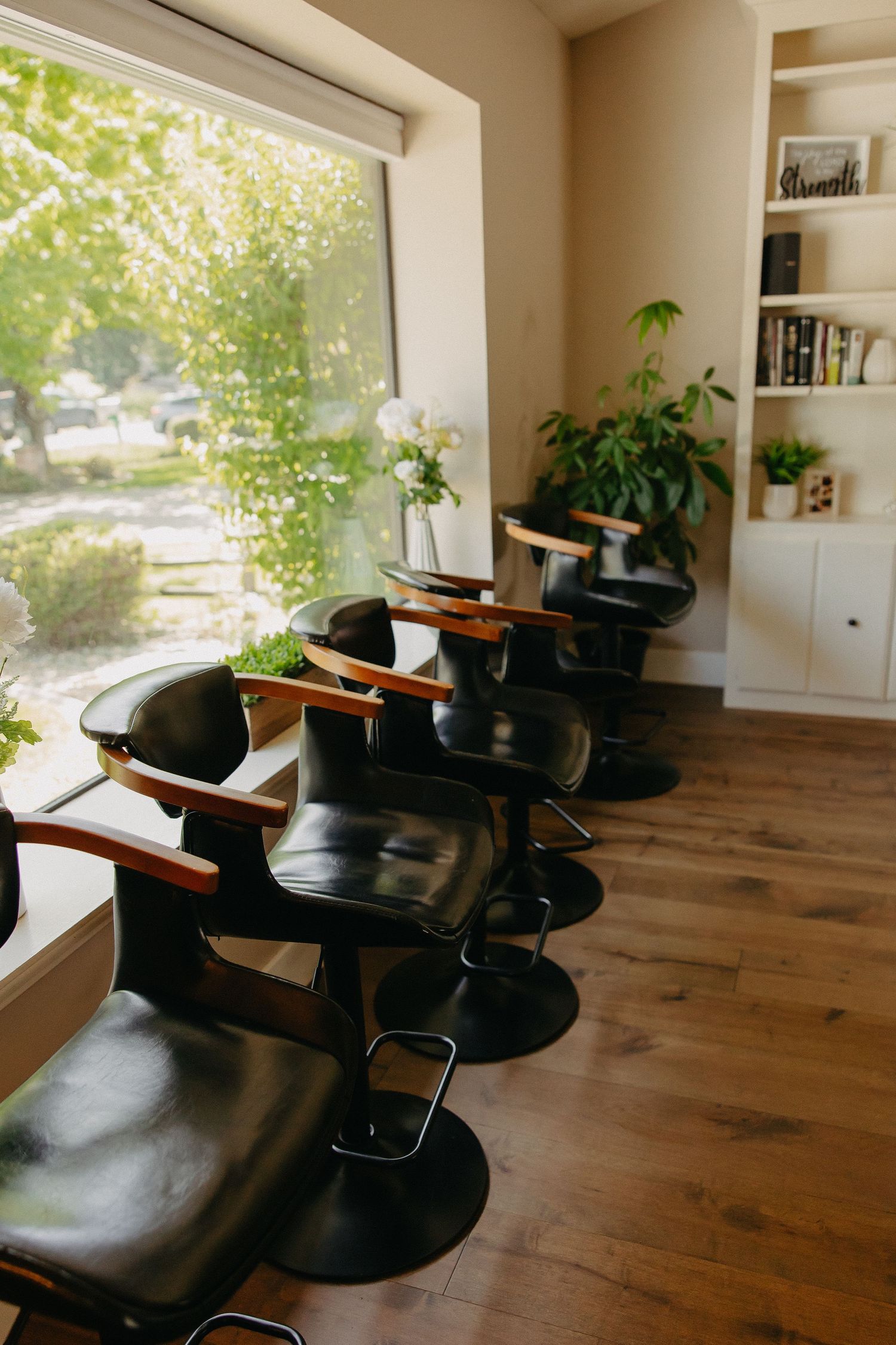 Row of salon styling chairs by large window with natural light and built-in bookshelf.