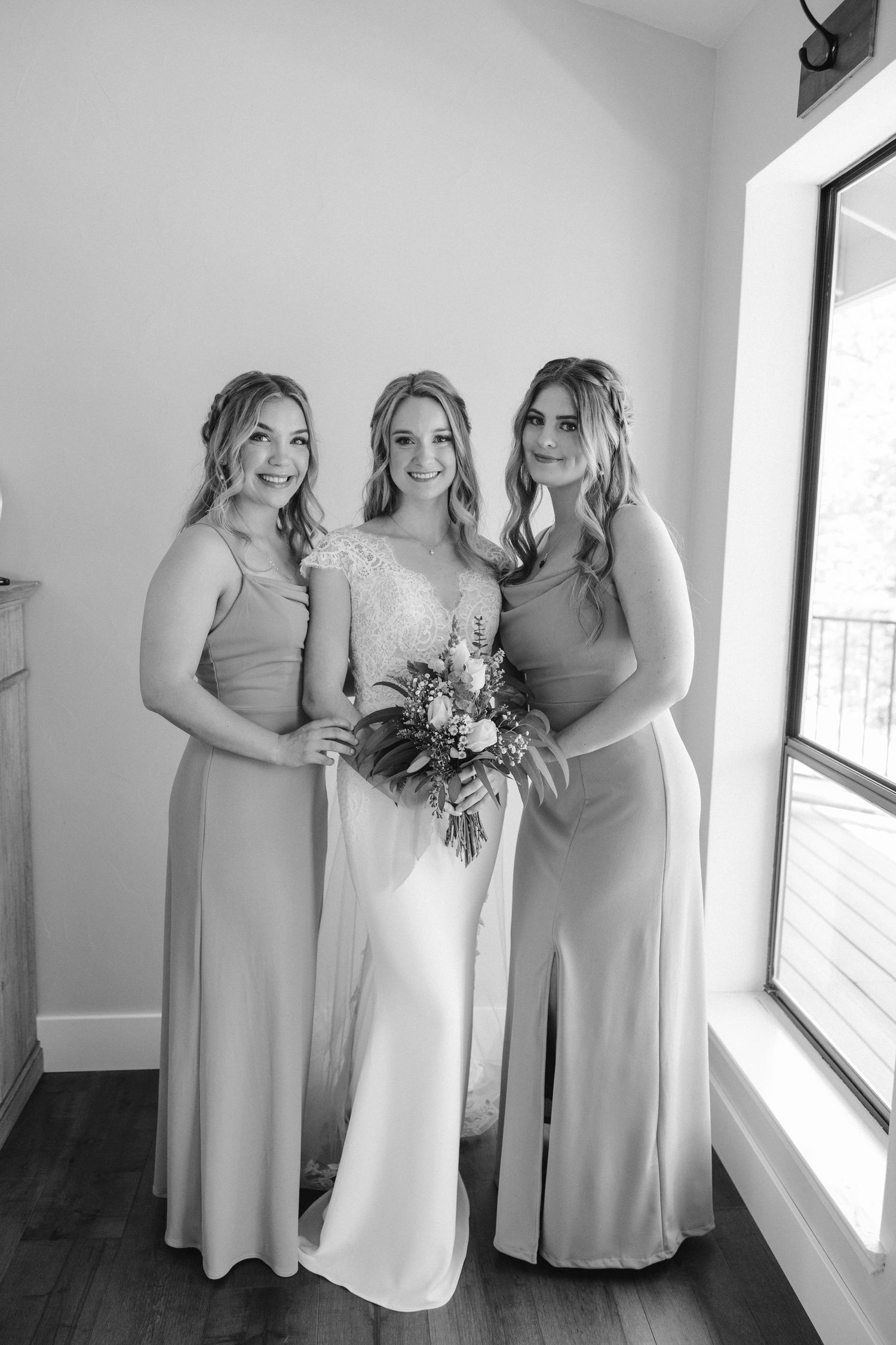 Black and white portrait of bride with bridesmaids in matching gowns holding floral bouquets.