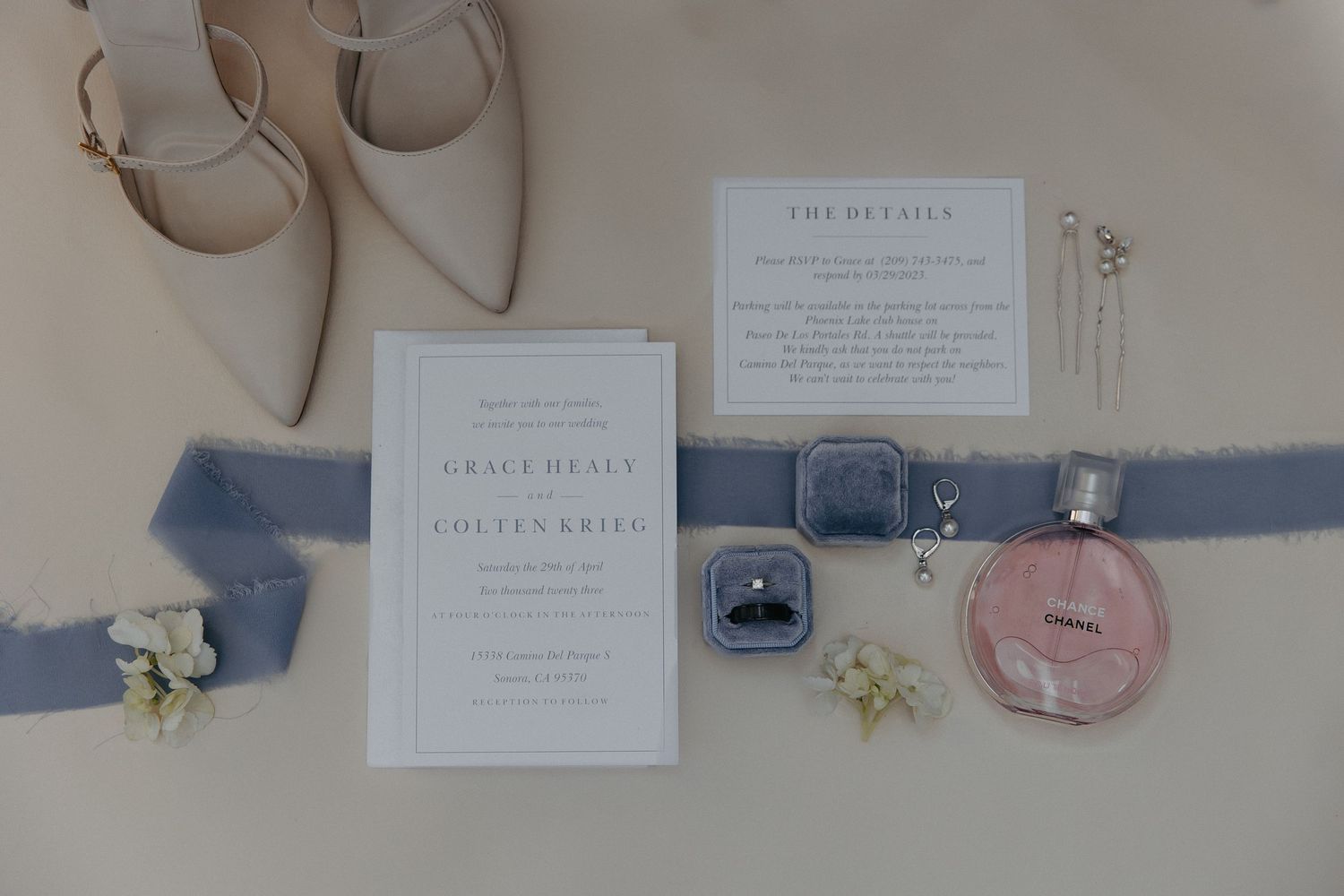 Wedding details flat lay with invitation, blue ribbon, nude shoes and delicate flowers.