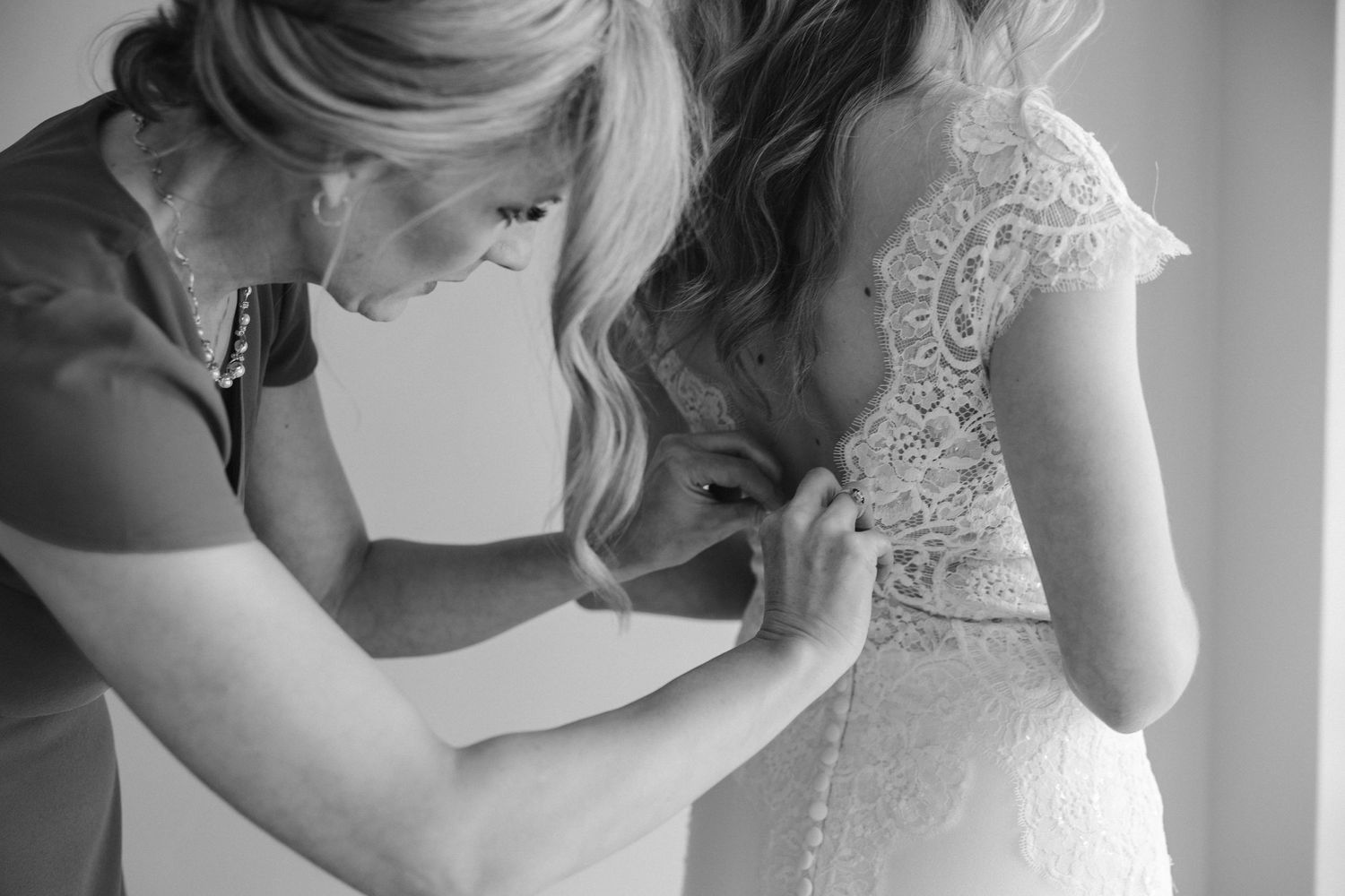 Black and white close-up of dress fitting moment showing intricate lace details.