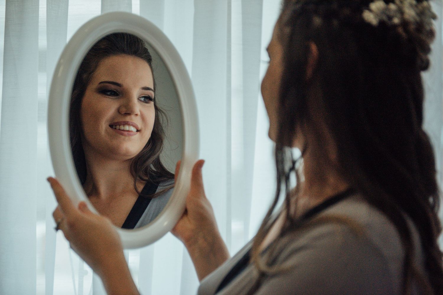 A reflection in an oval mirror shows someone getting ready for a special occasion.