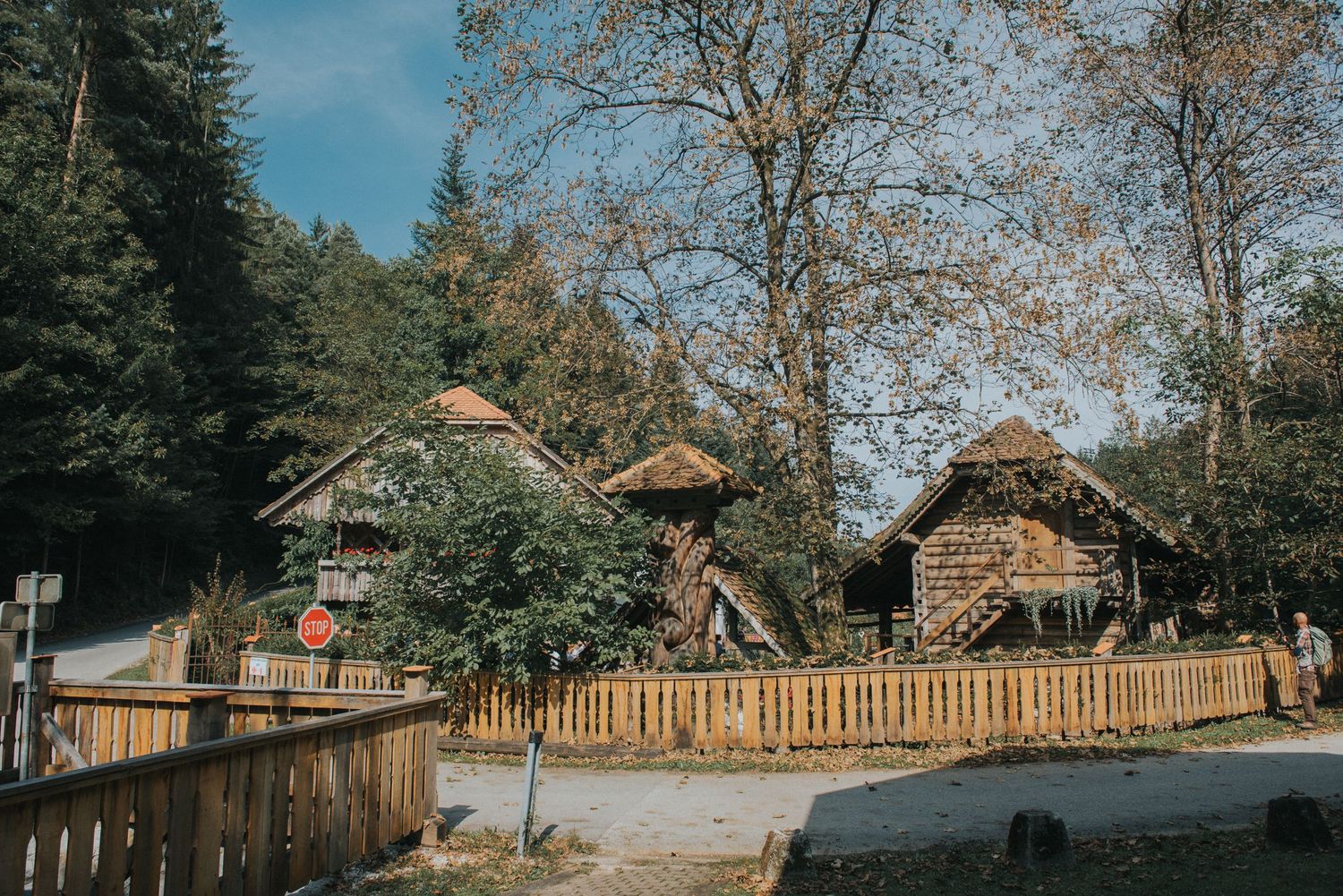 Rustic wooden cabins with thatched roofs surrounded by trees and wooden fencing at a countryside venue.