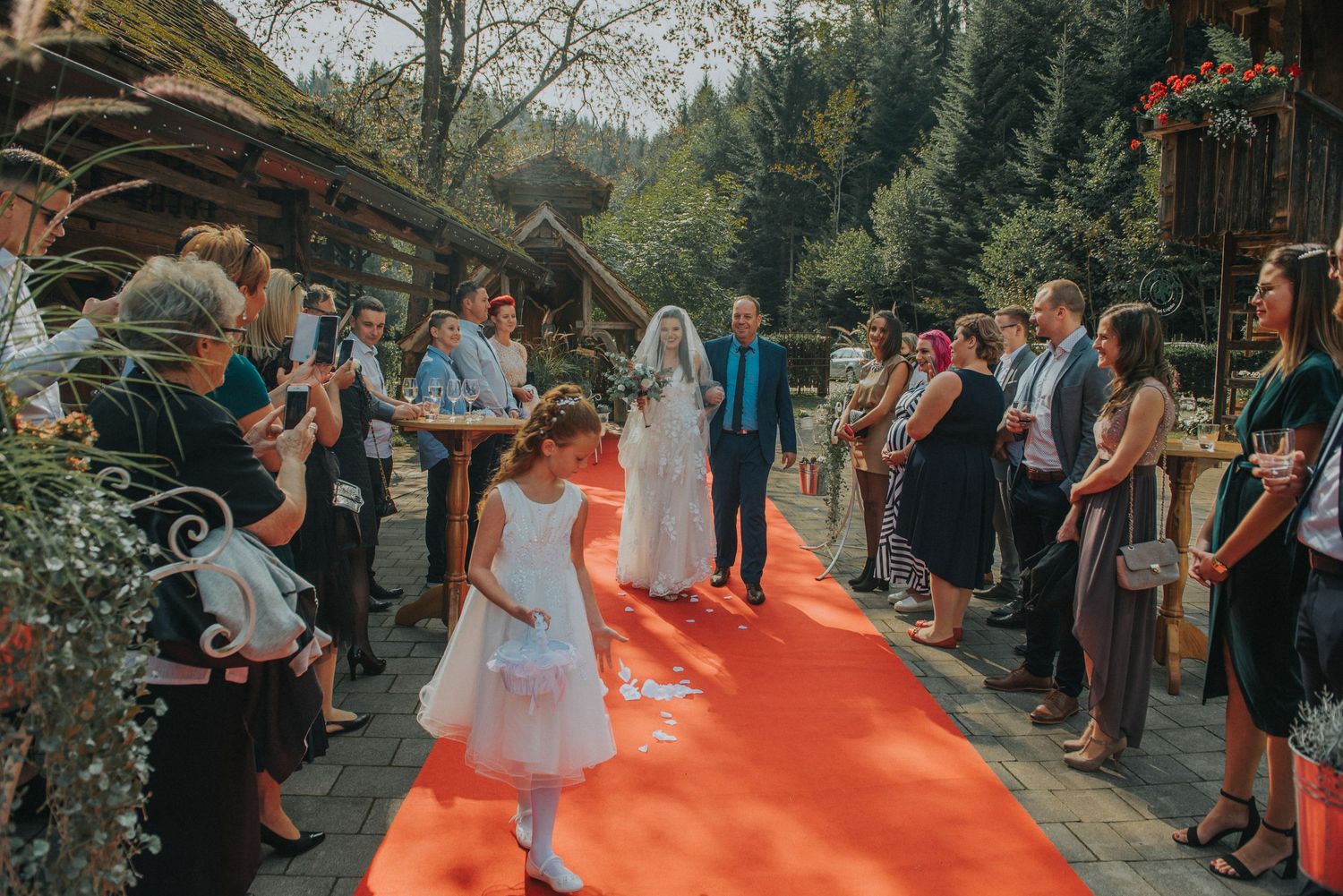 Wedding ceremony outdoors with guests lined up along a red carpet aisle.