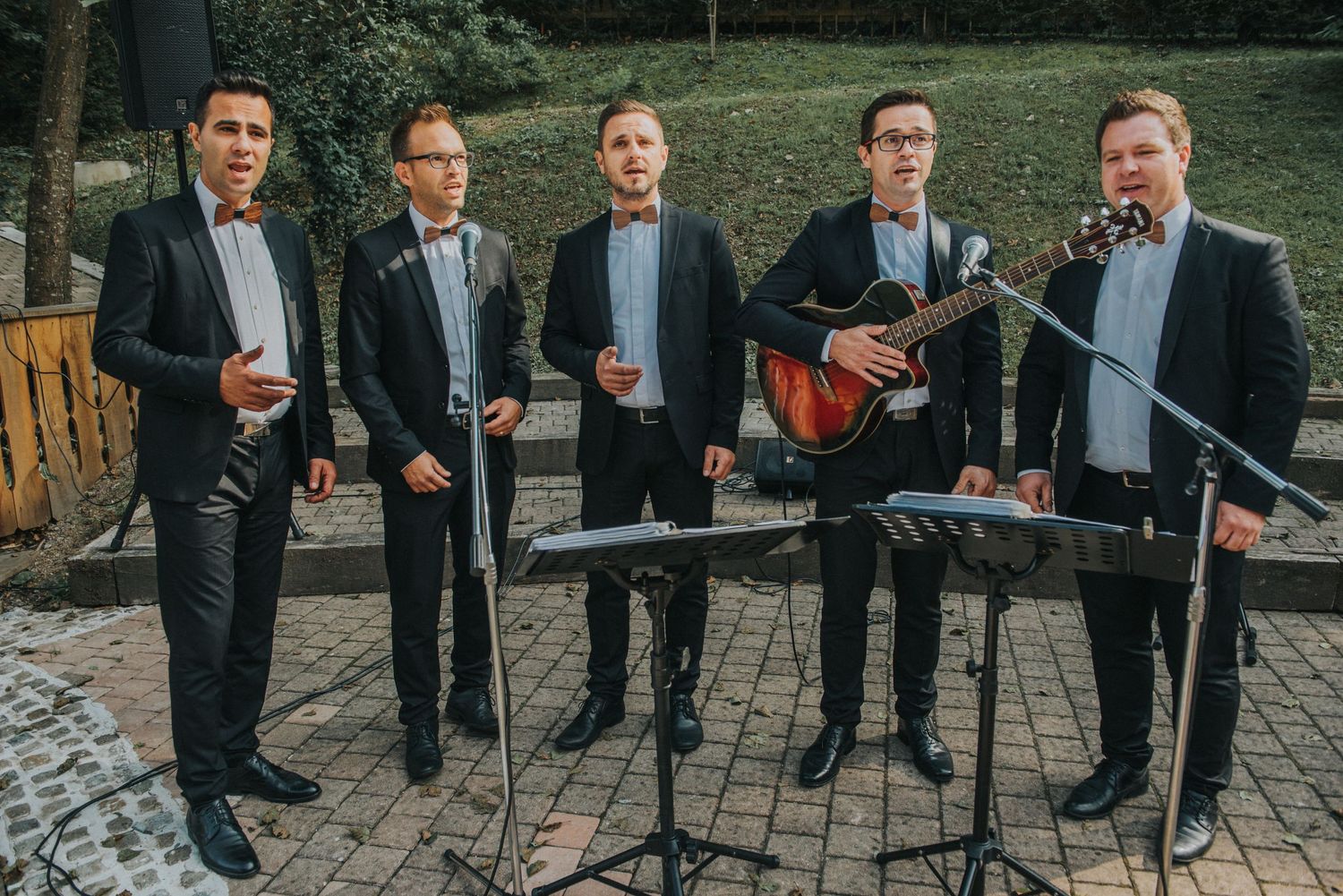 A five-piece band in formal attire performs with musical instruments on a brick patio.