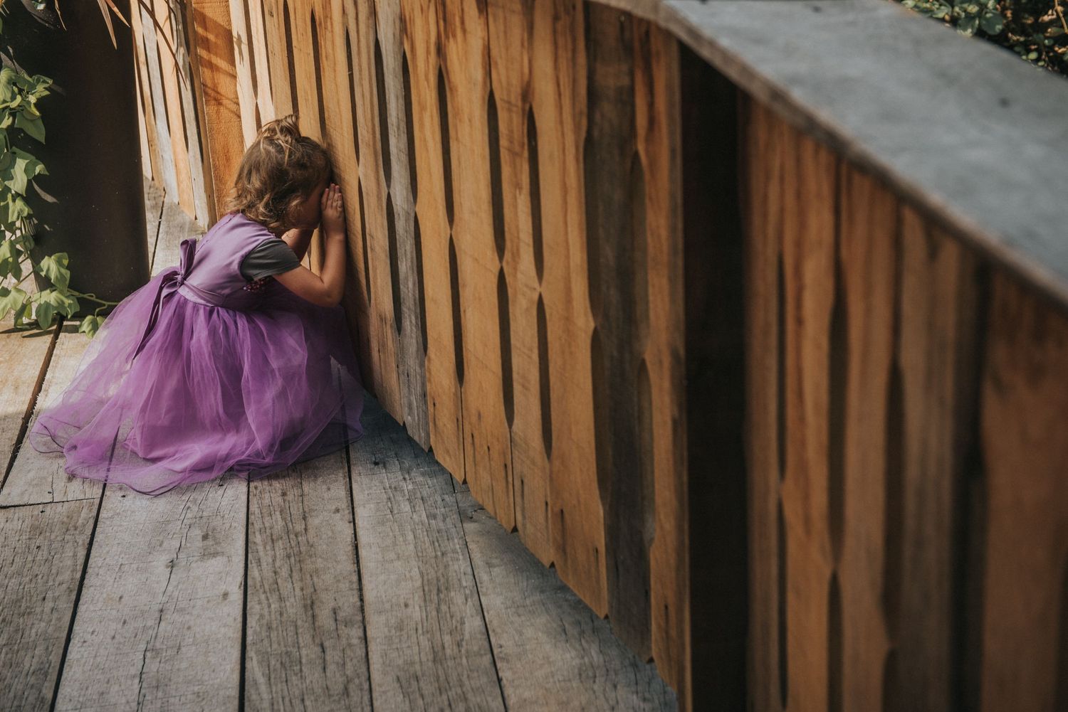 A child in a purple dress sits beside a wooden railing.