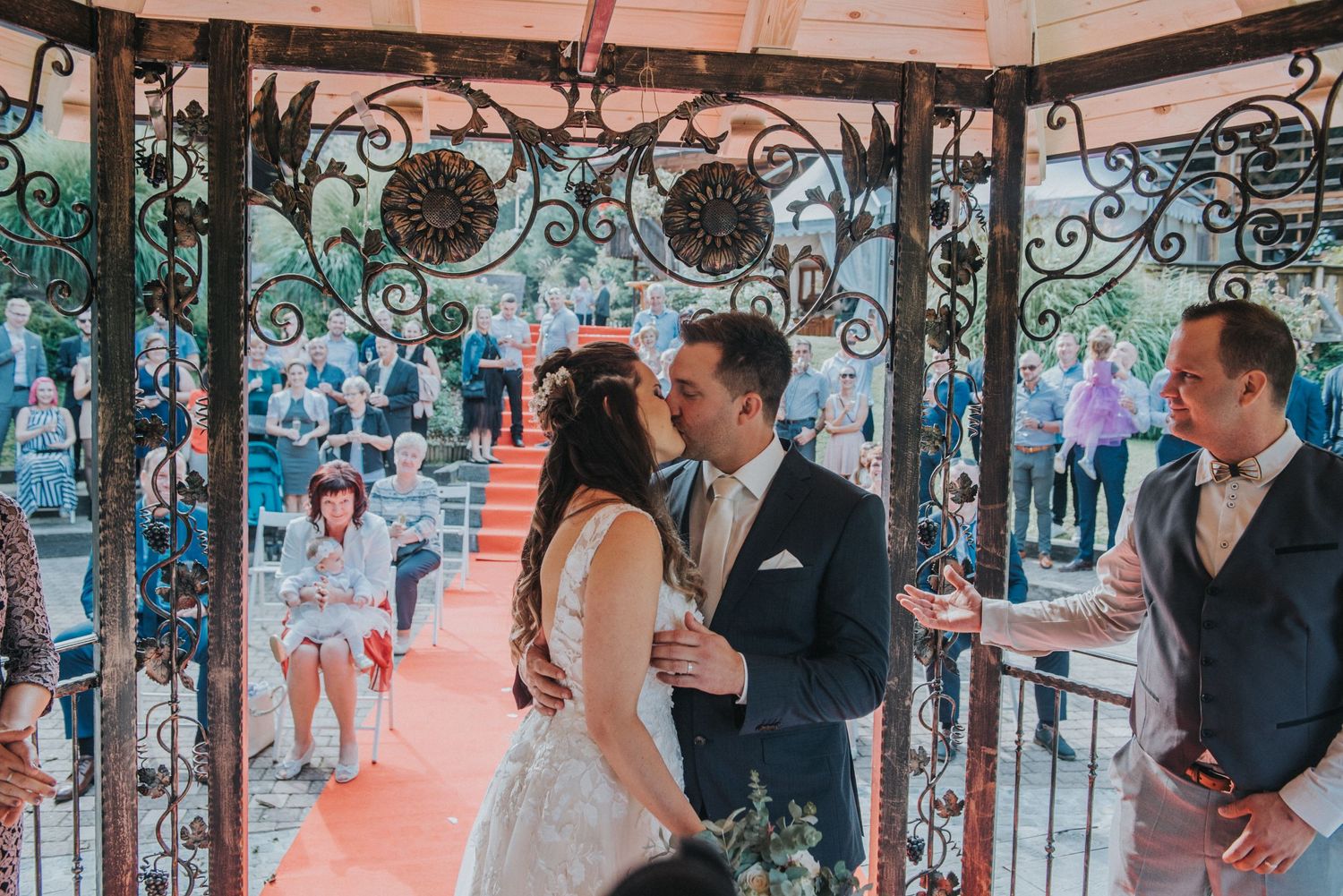 A couple shares an intimate moment during their wedding ceremony in a decorated gazebo.