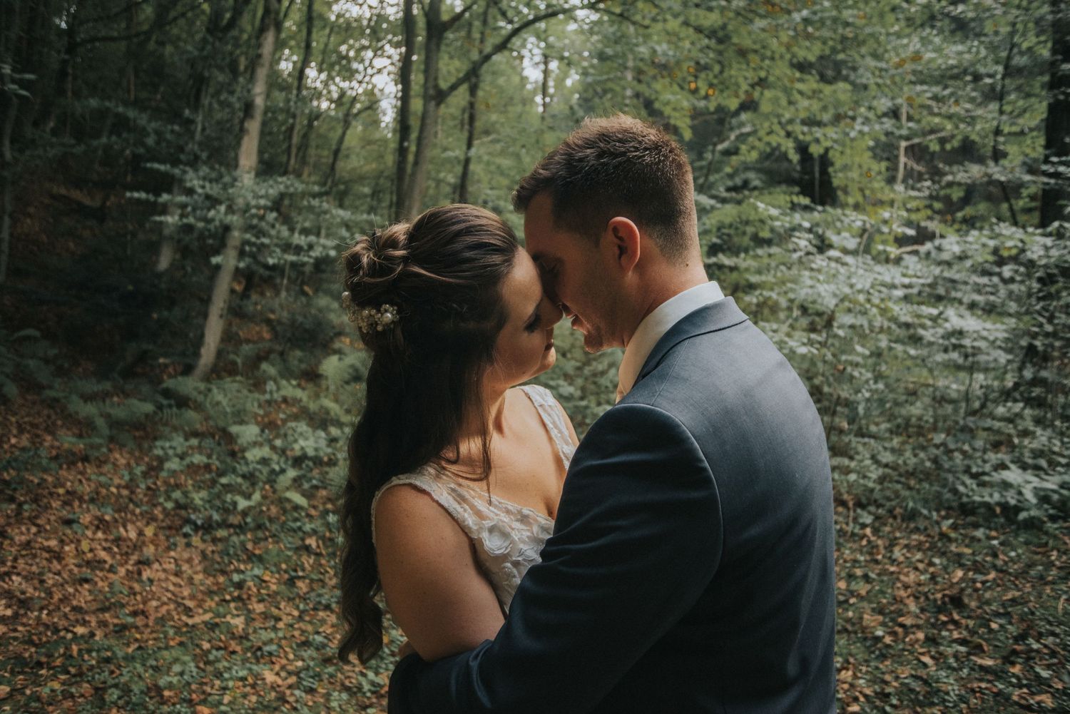 Intimate moment captured in moody forest setting with autumn leaves.
