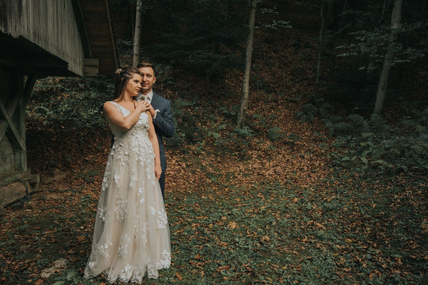 Elegant wedding portrait in moody forest setting with rustic cabin backdrop.