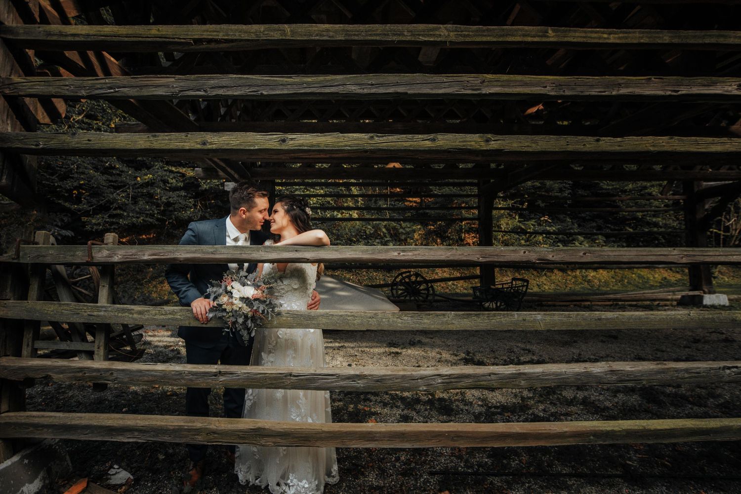 A romantic wedding photo through rustic wooden slats creates a dramatic framing effect in natural lighting.Hiša Lisjak