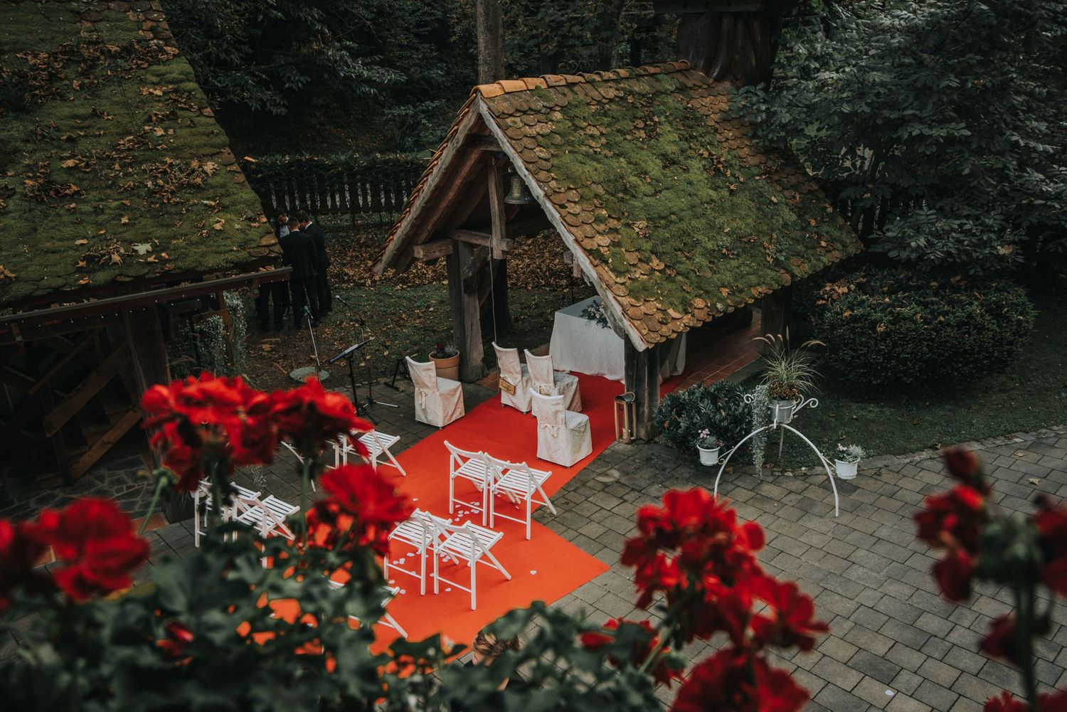 A rustic wooden gazebo decorated for a wedding ceremony with red flowers and white chairs.