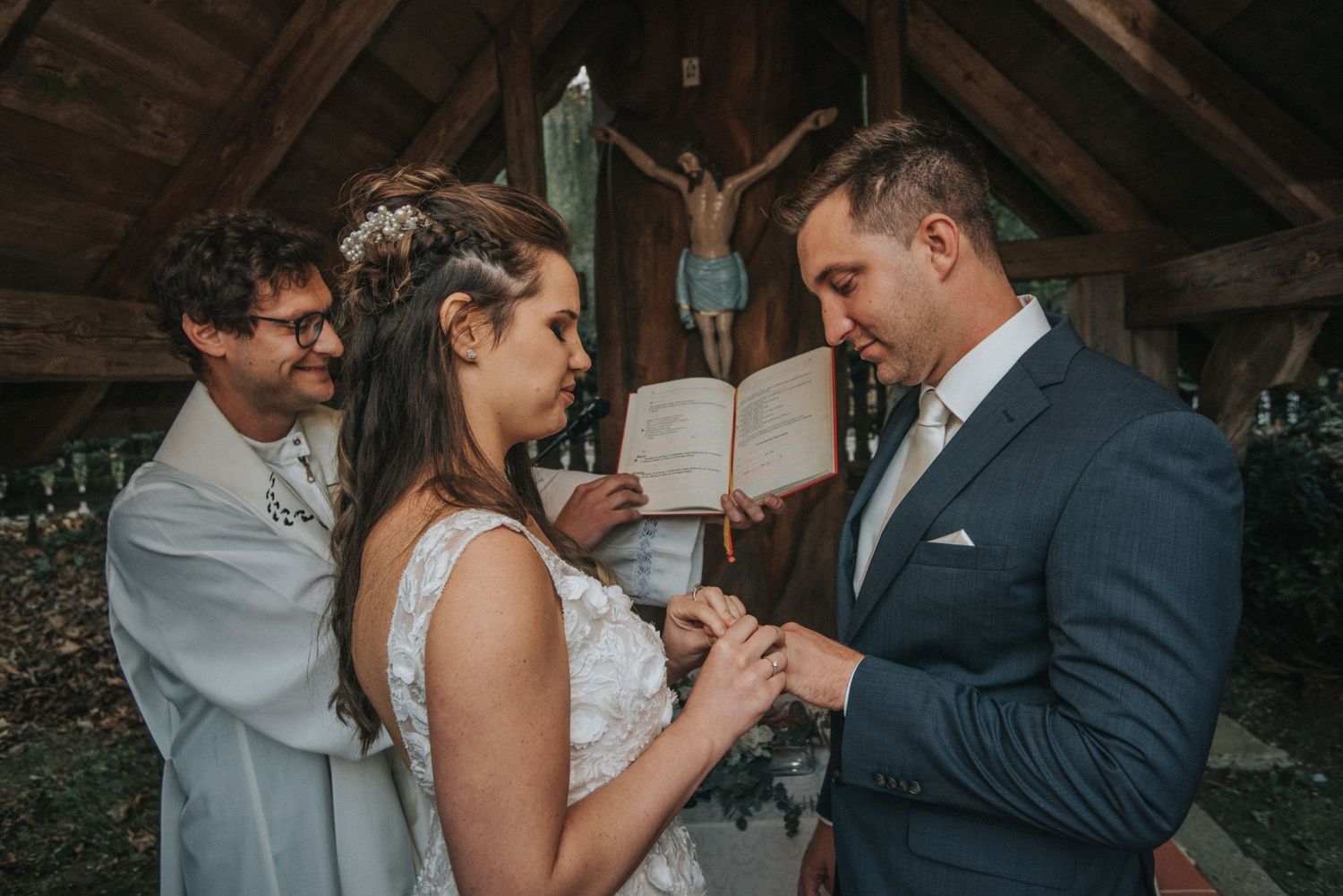 Intimate wedding ceremony moment under wooden beams with crucifix in background.