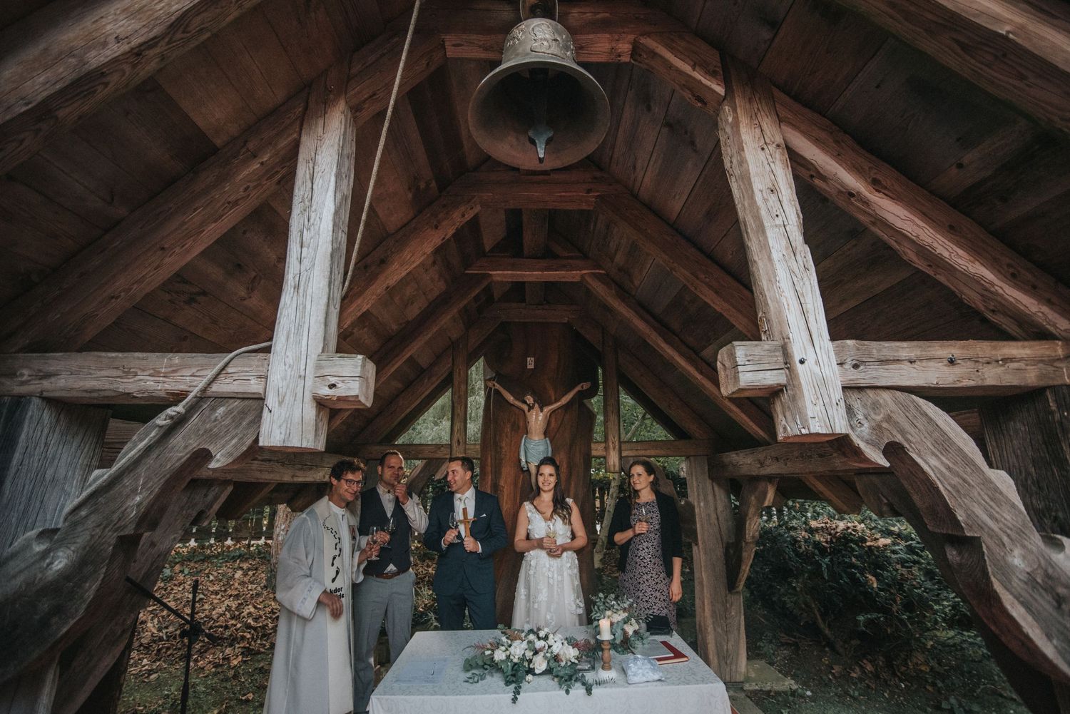 Rustic chapel interior with exposed wooden beams and hanging bells during ceremony.
