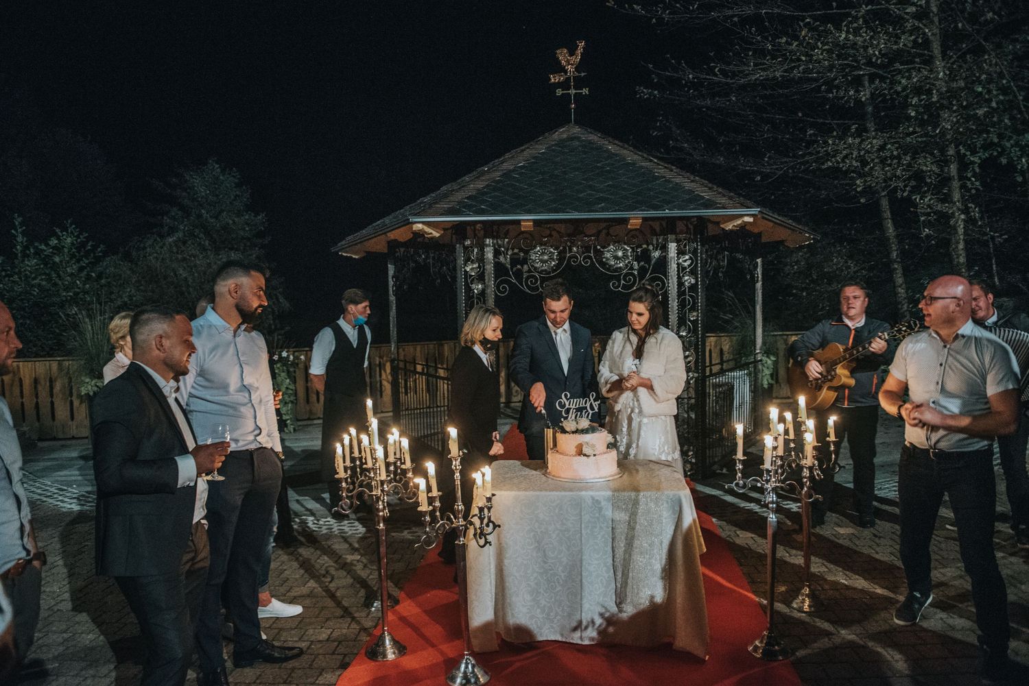 Nighttime wedding ceremony at gazebo decorated with candlelight and red carpet.