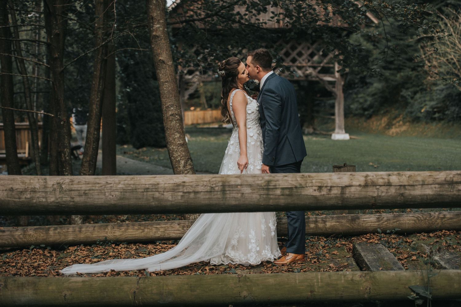 A couple shares an intimate moment on a rustic wooden bridge surrounded by autumn trees.
