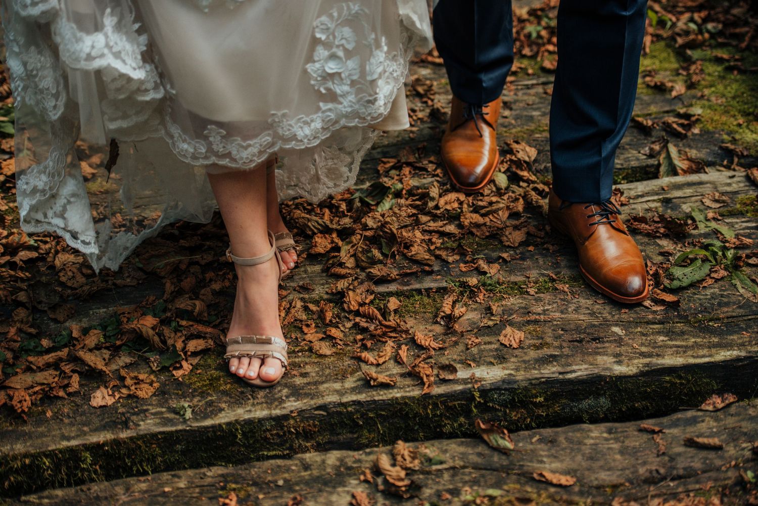 Close-up of feet on stone steps with autumn leaves, showing one foot in brown leather shoe and another barefoot in lace dress. Hiša Lisjak