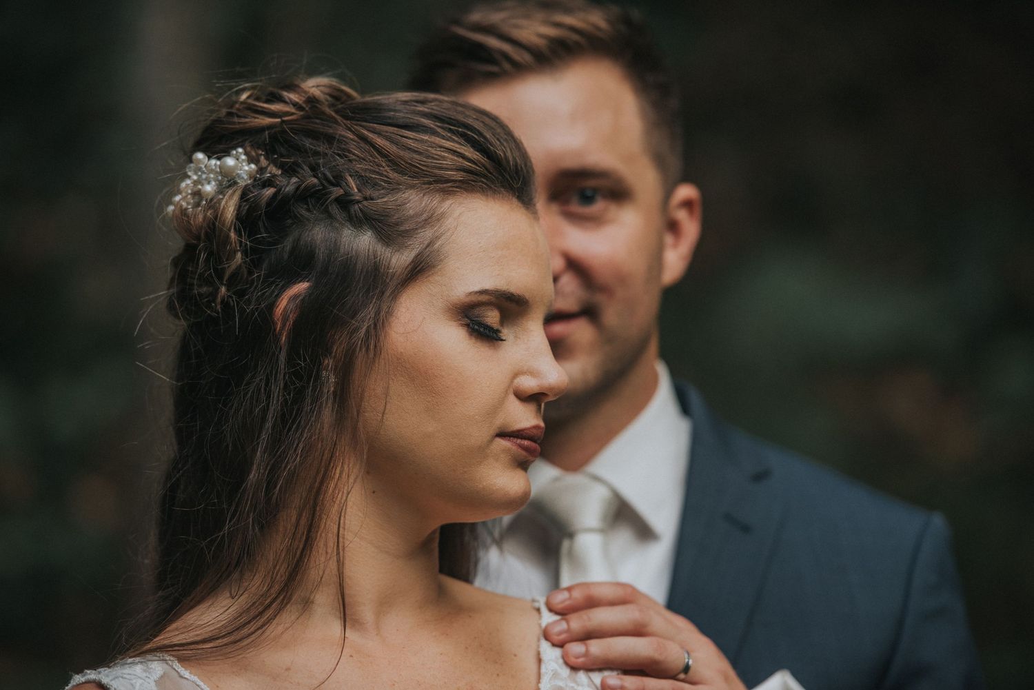 A close-up wedding portrait showing tender intimacy between newlyweds in a forest setting.