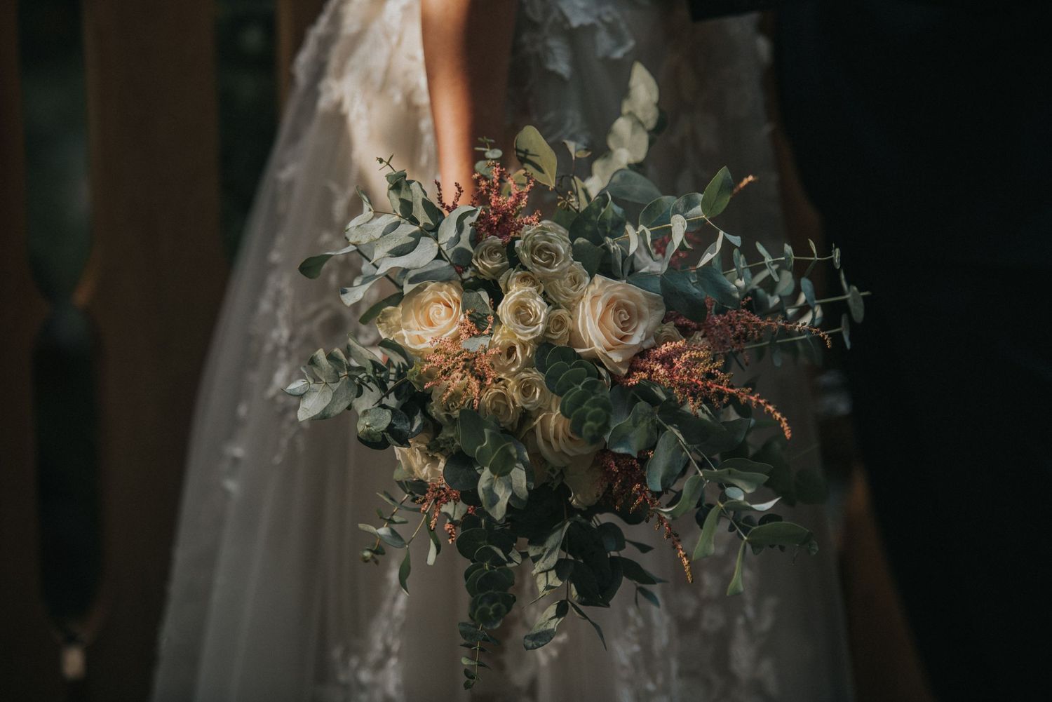 An elegant bridal bouquet with roses and eucalyptus against a white wedding dress.