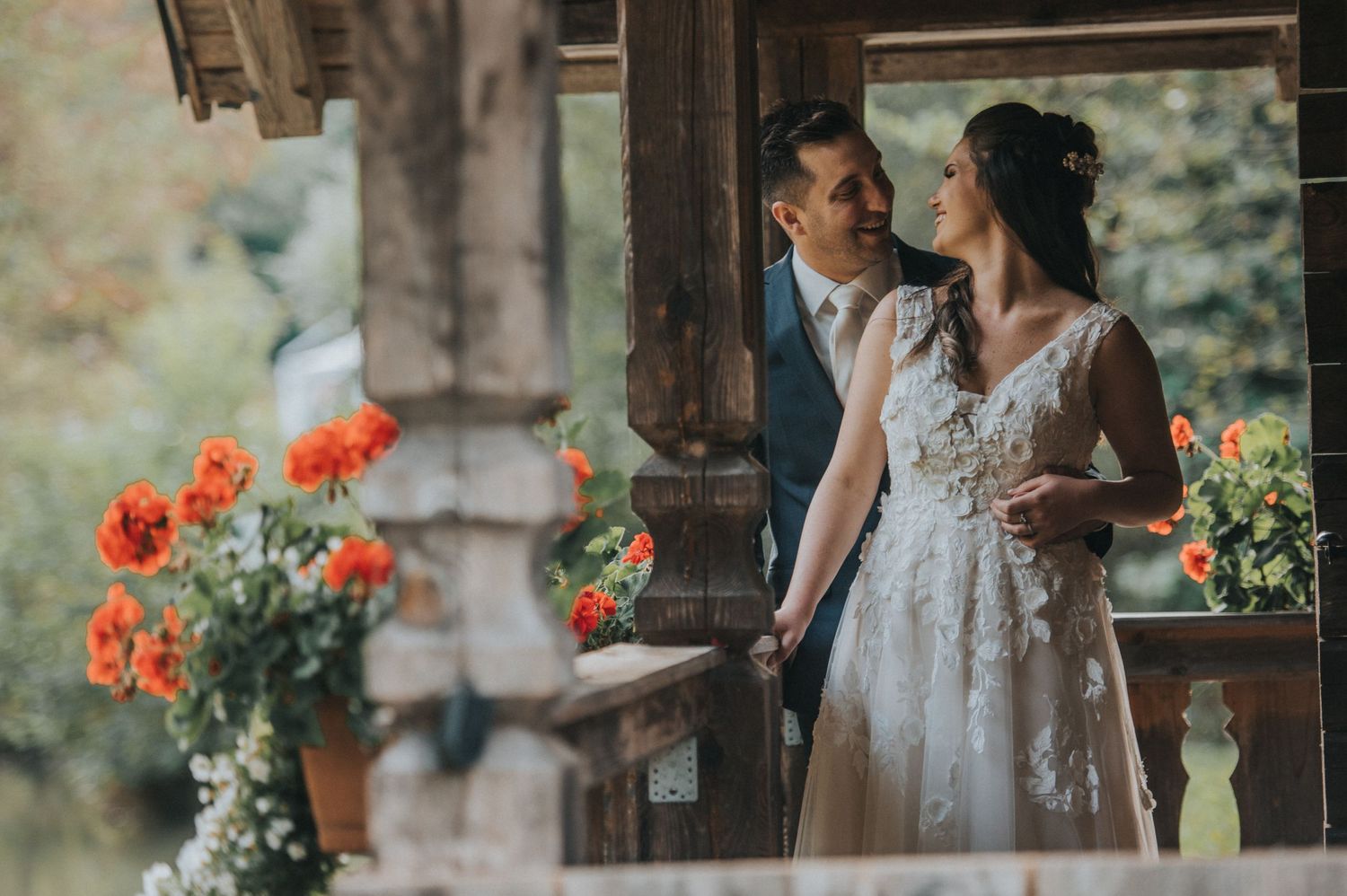 A romantic wedding scene with bright orange flowers in a rustic wooden gazebo setting.