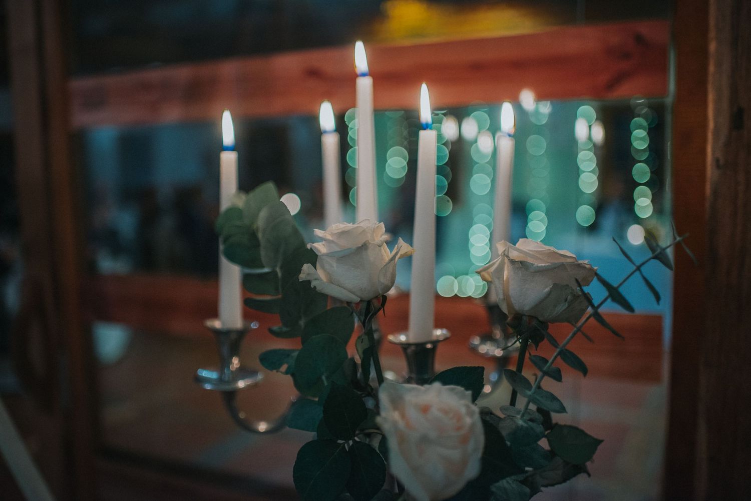 Elegant white candles and floral centerpiece arrangements on wedding reception table.