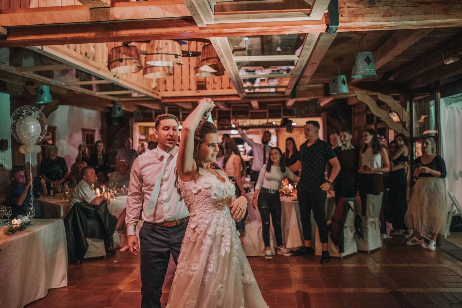 Wedding reception dance in rustic venue with wooden beams and warm lighting.
