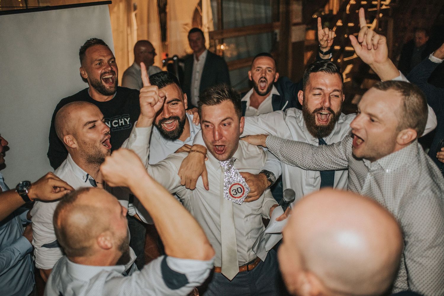 Groomsmen celebrating energetically at indoor wedding reception.