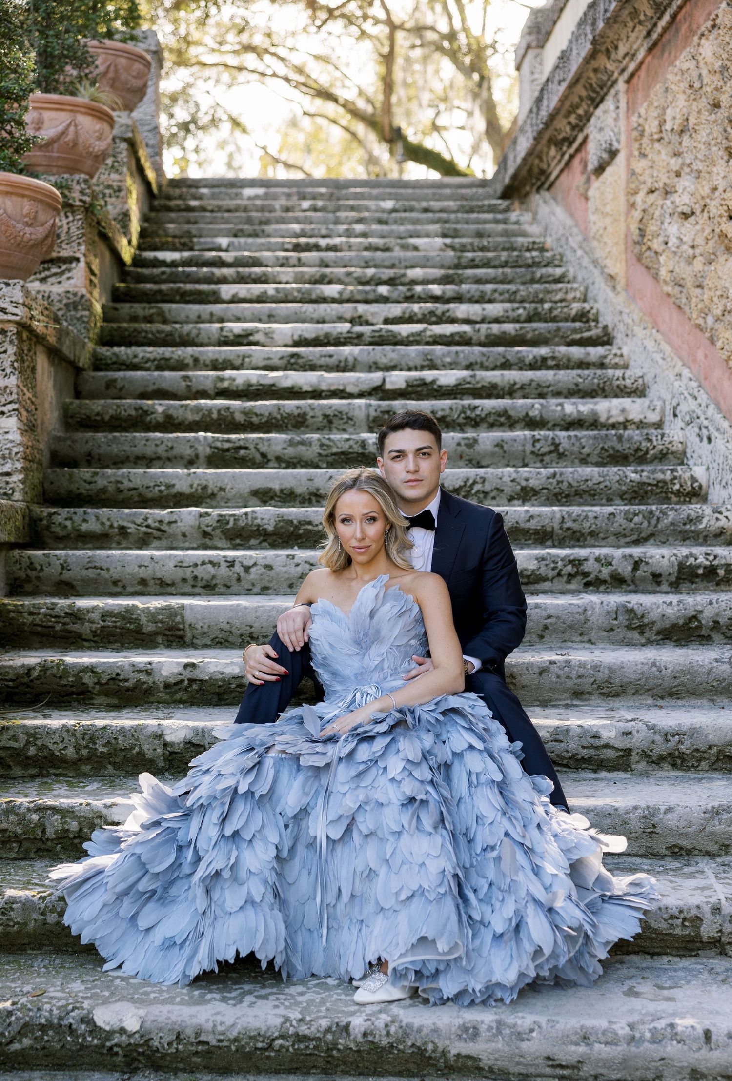 A romantic portrait on weathered stone steps featuring a dramatic light blue ball gown.