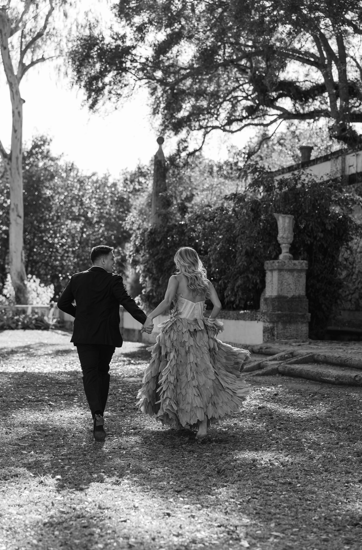 Black and white image of a couple running through a garden path surrounded by trees.